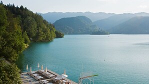 A lakeside resort with sun loungers and umbrellas, a dock, and a view of the lake and surrounding hills. - Grand Hotel Toplice - Sava Hotels & Resorts (Bled)