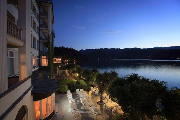 A lakeside hotel patio with outdoor seating and a view of the lake and mountains.