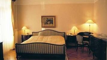 A hotel room with a bed, a desk, two lamps, a chair, and a painting on the wall.