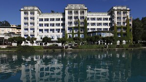 A multi-story hotel with balconies, a reflective pool in front, and a clear blue sky. - Grand Hotel Toplice - Sava Hotels & Resorts (Bled)