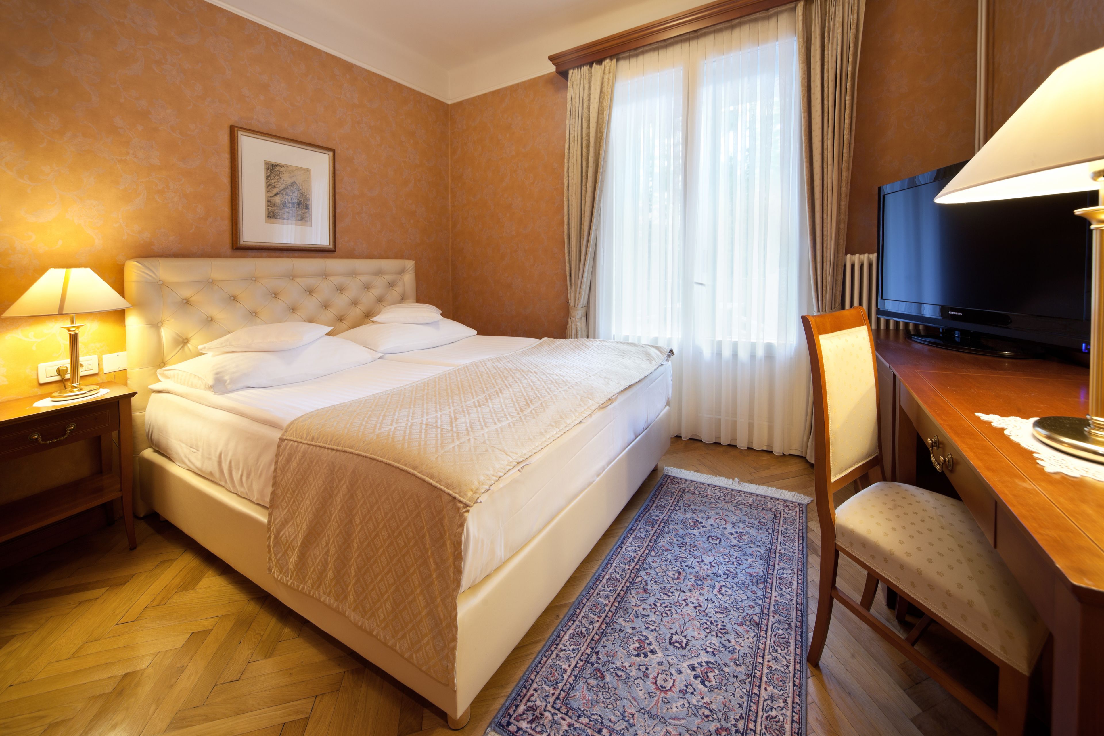 Una habitación de hotel con una cama grande, un escritorio con una silla, un televisor y una ventana con cortinas.