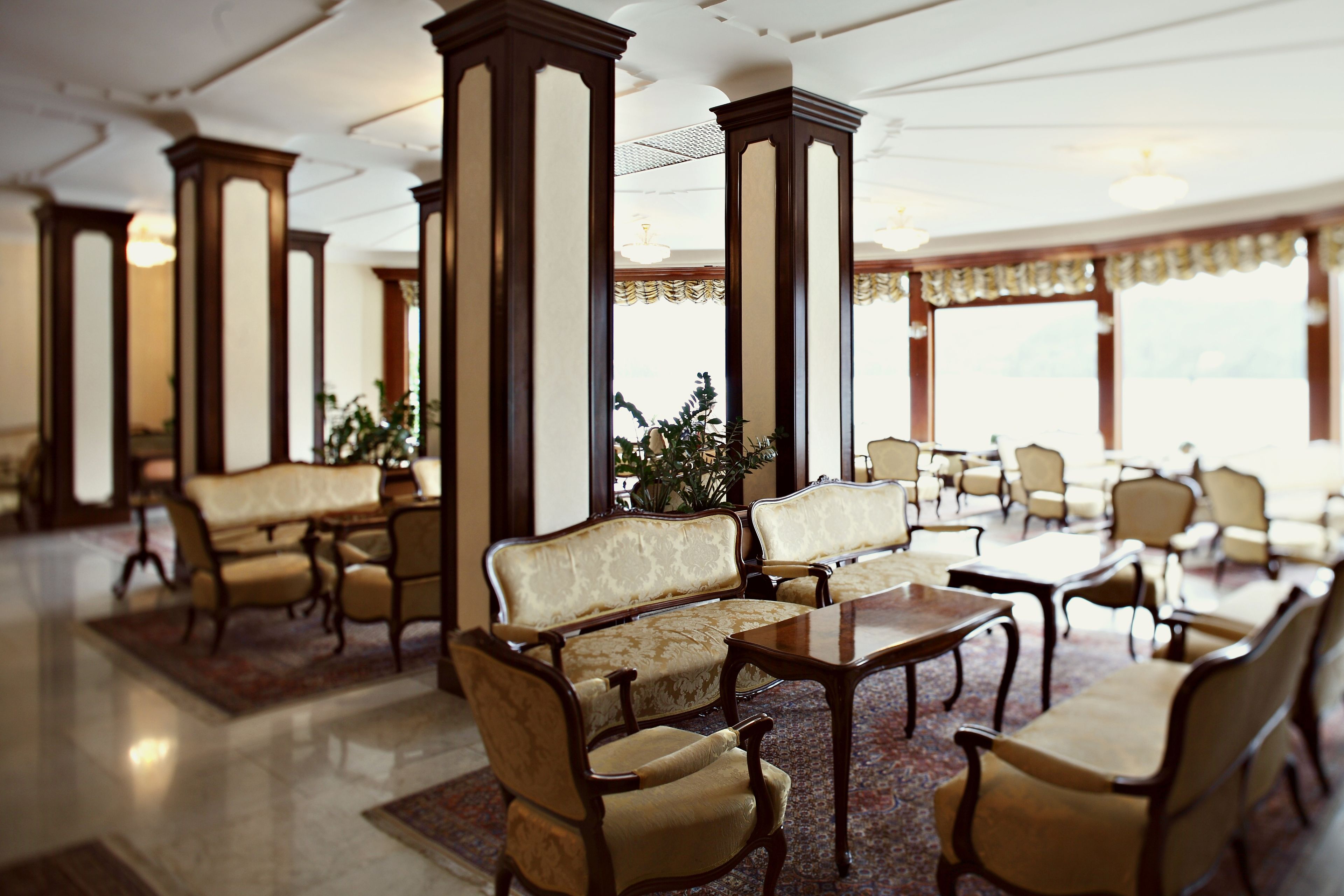 A hotel lobby with a classic design, featuring high wooden columns, plush seating, and a large window providing natural light.
