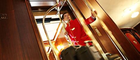 A hotel interior with a wooden floor, a luggage cart, and a person in a red uniform.