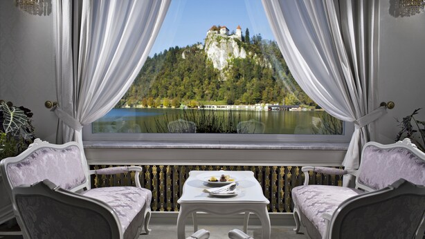 A balcony with two chairs and a table, overlooking a lake and a castle. - Grand Hotel Toplice - Sava Hotels & Resorts (Bled)