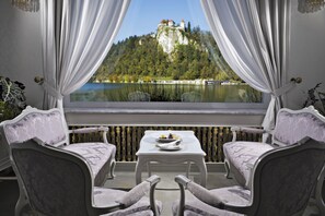 A balcony with two chairs and a table, overlooking a lake and a castle.
