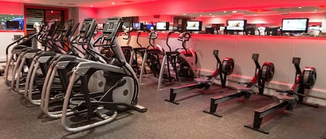 Un gimnasio con varias cintas de correr y máquinas elípticas, dispuestas en filas.