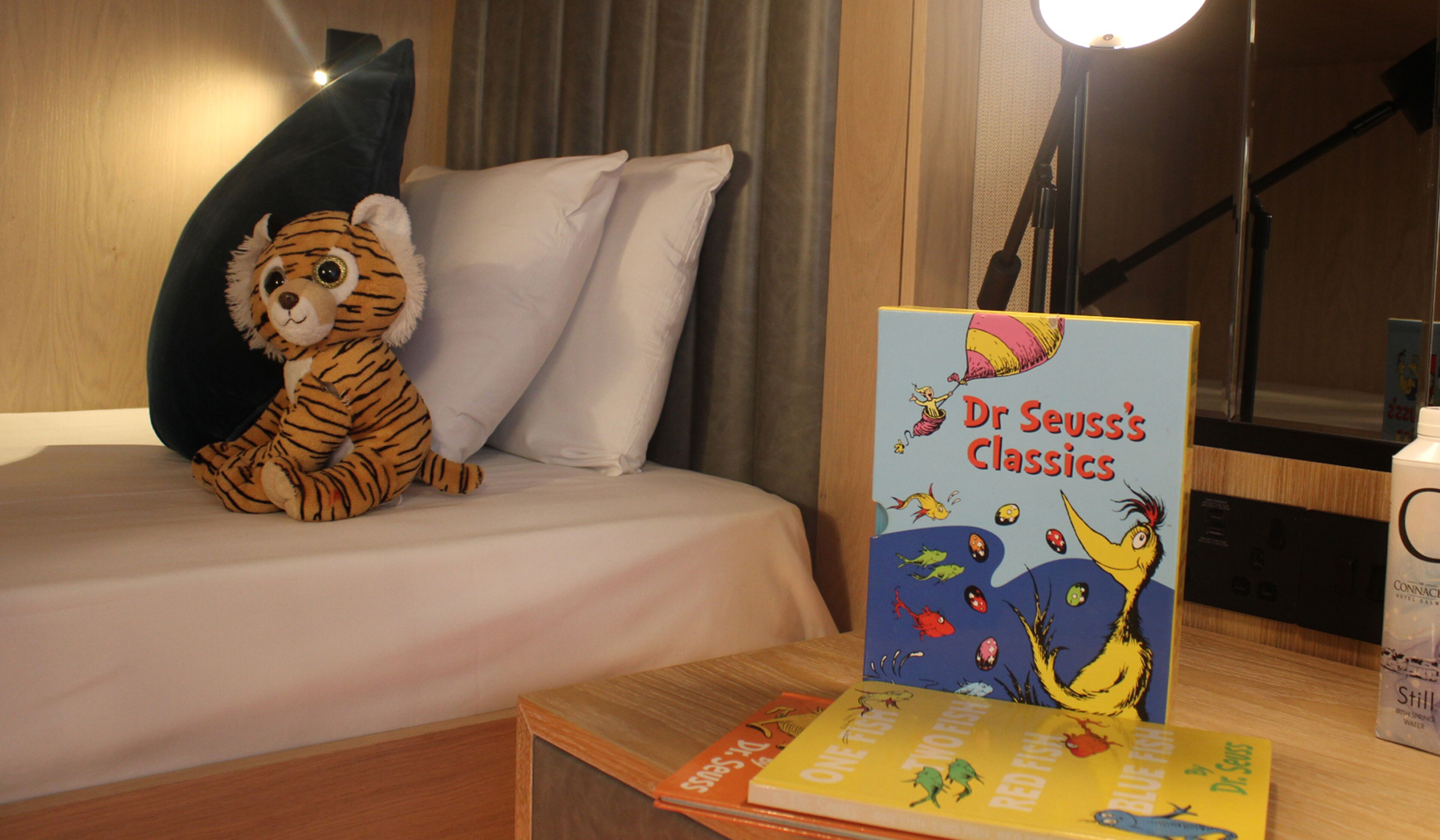 A hotel room with a bed, a plush tiger toy, and a Dr. Seuss book titled 'One Fish Two Fish Red Fish Blue Fish'.