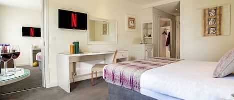 A hotel room with a bed, a desk, a chair, a TV, and a small table with wine glasses.