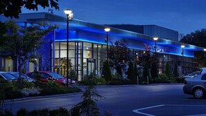 Un hotel moderno con fachada de vidrio, estacionamiento y farolas.