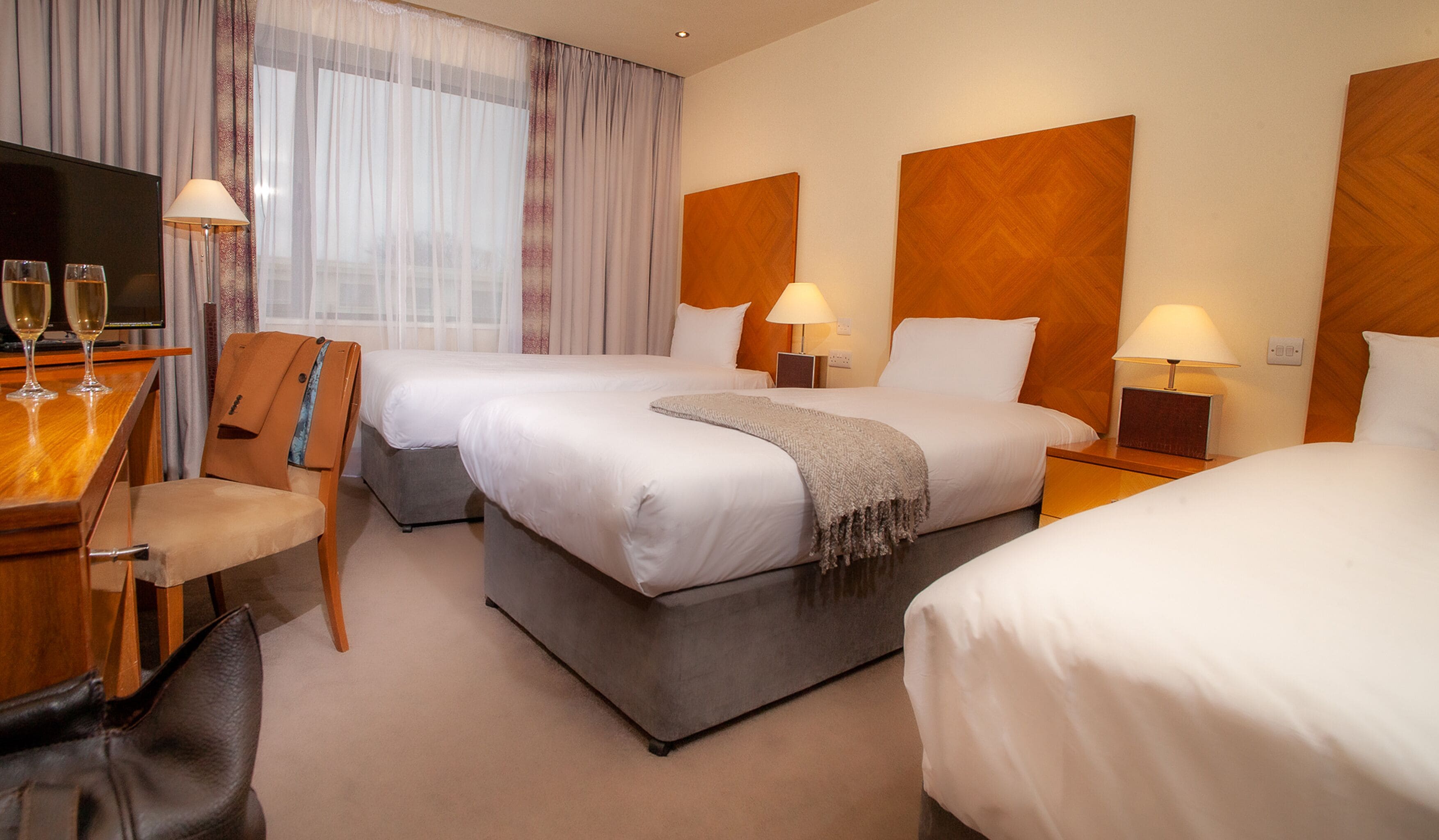 Une chambre d’hôtel avec deux lits, un bureau avec deux verres de vin, une chaise et une télévision.