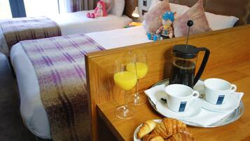 Een hotelkamer met twee bedden, een ontbijtserver met croissants, sap, koffie en bekers, en uitzicht op de kamer.