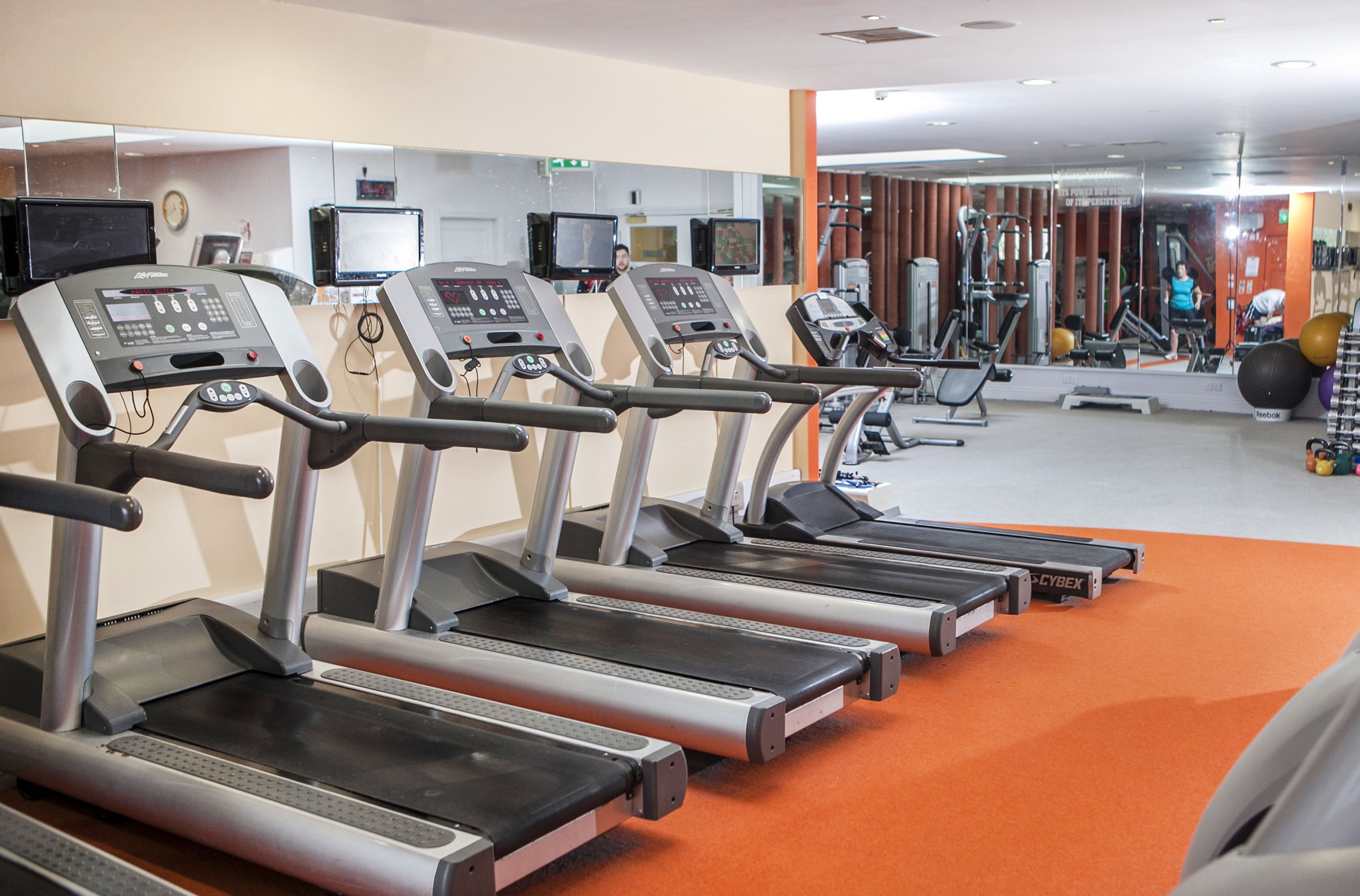 A gym with treadmills, exercise equipment, and a mirror wall.