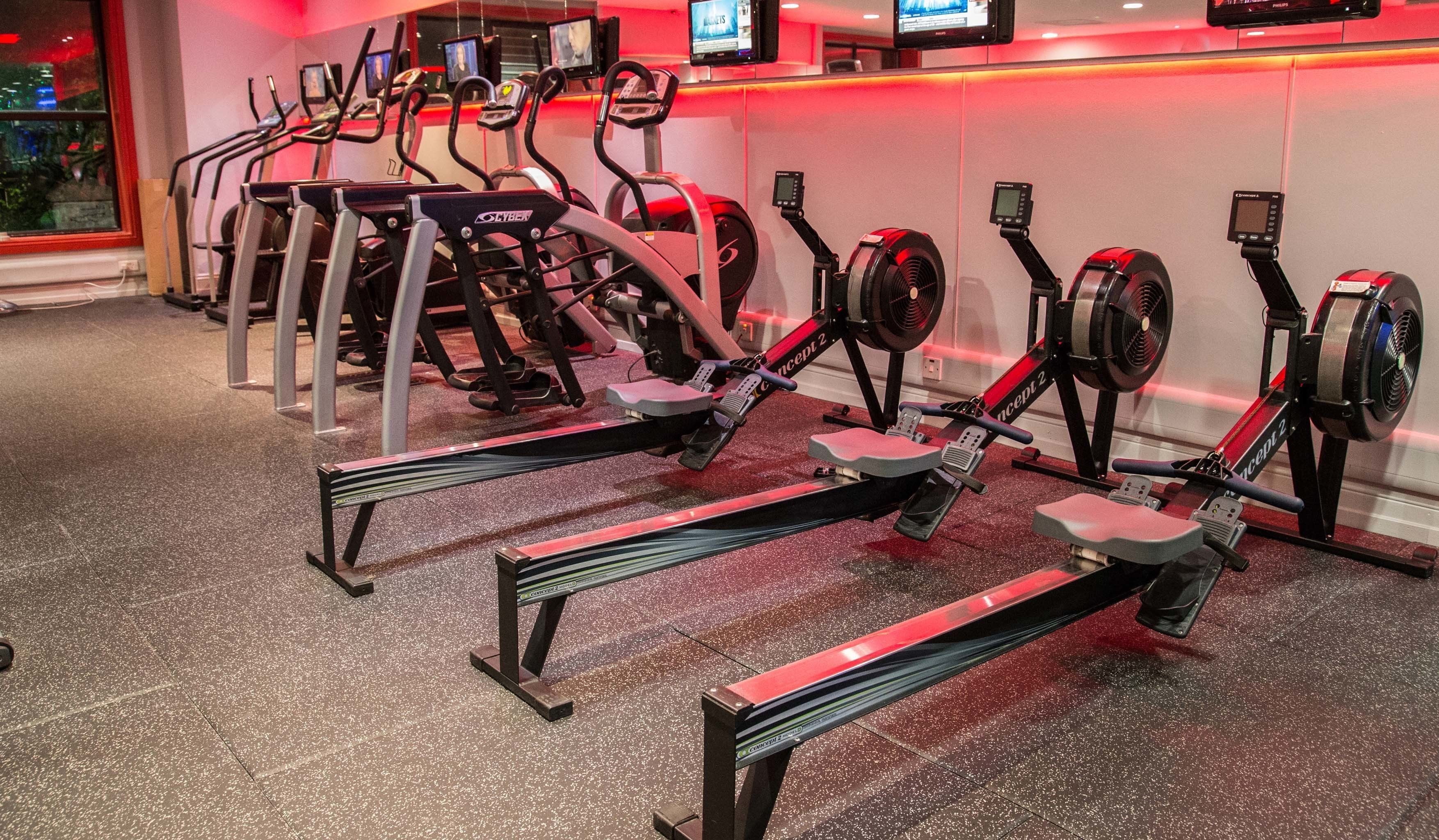 Une salle de sport équipée de nombreux appareils de cardio, notamment des tapis de course et des vélos elliptiques, disposés en rangées.