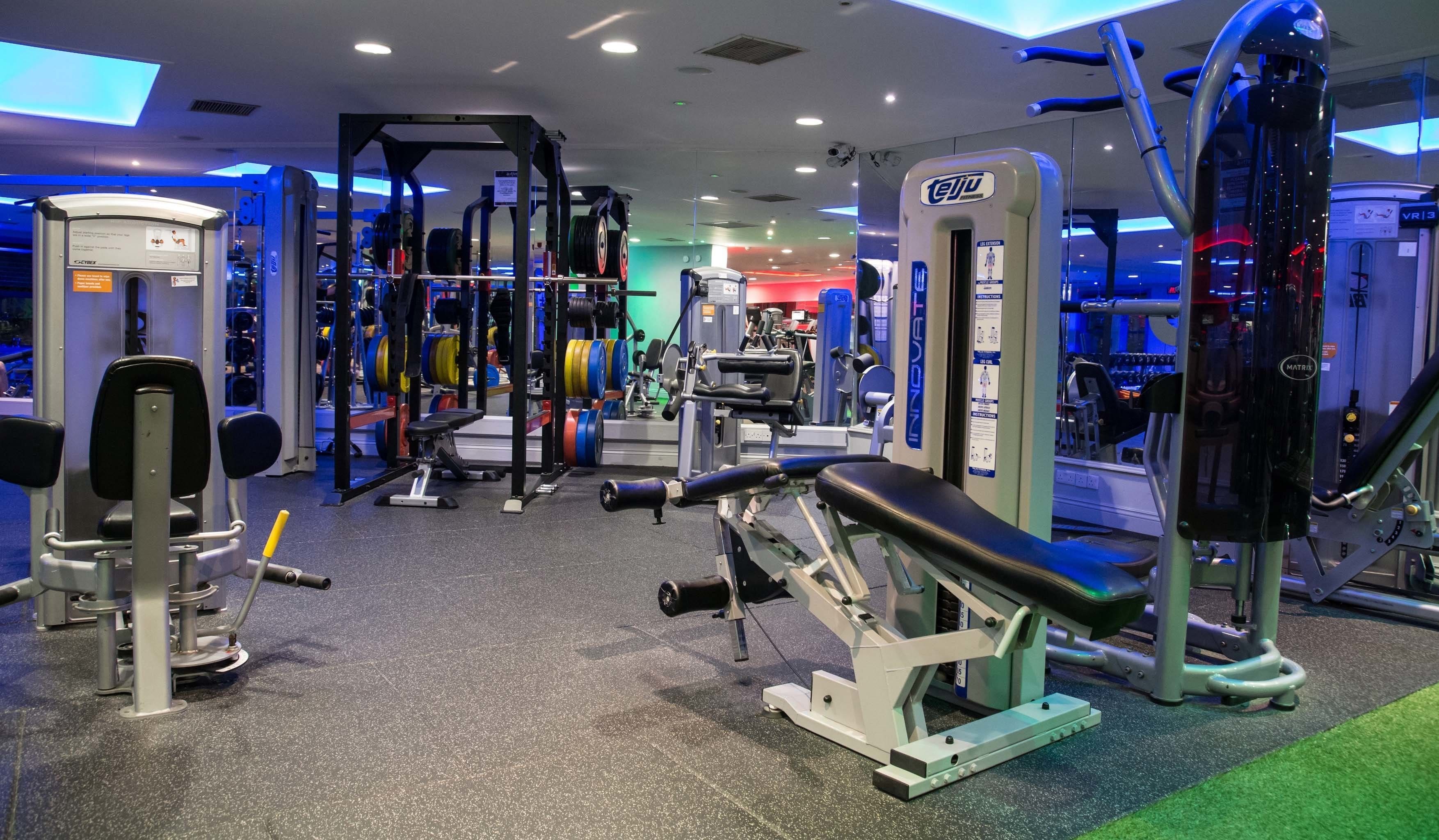 Un gimnasio con diverso equipo de ejercicio, que incluye máquinas de pesas, pesas libres y máquinas de cardio.