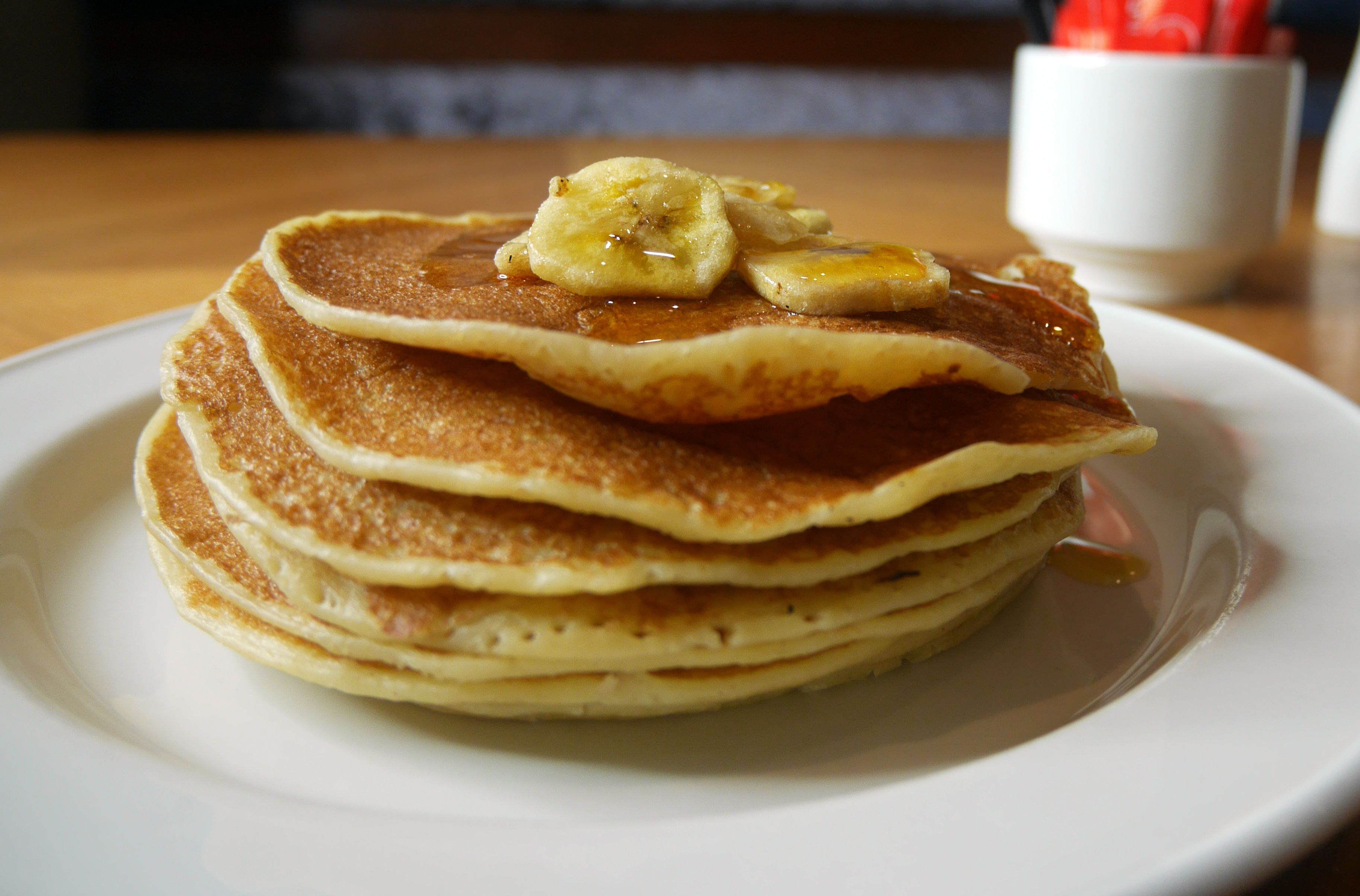 A stack of pancakes with banana slices and syrup on a white plate.