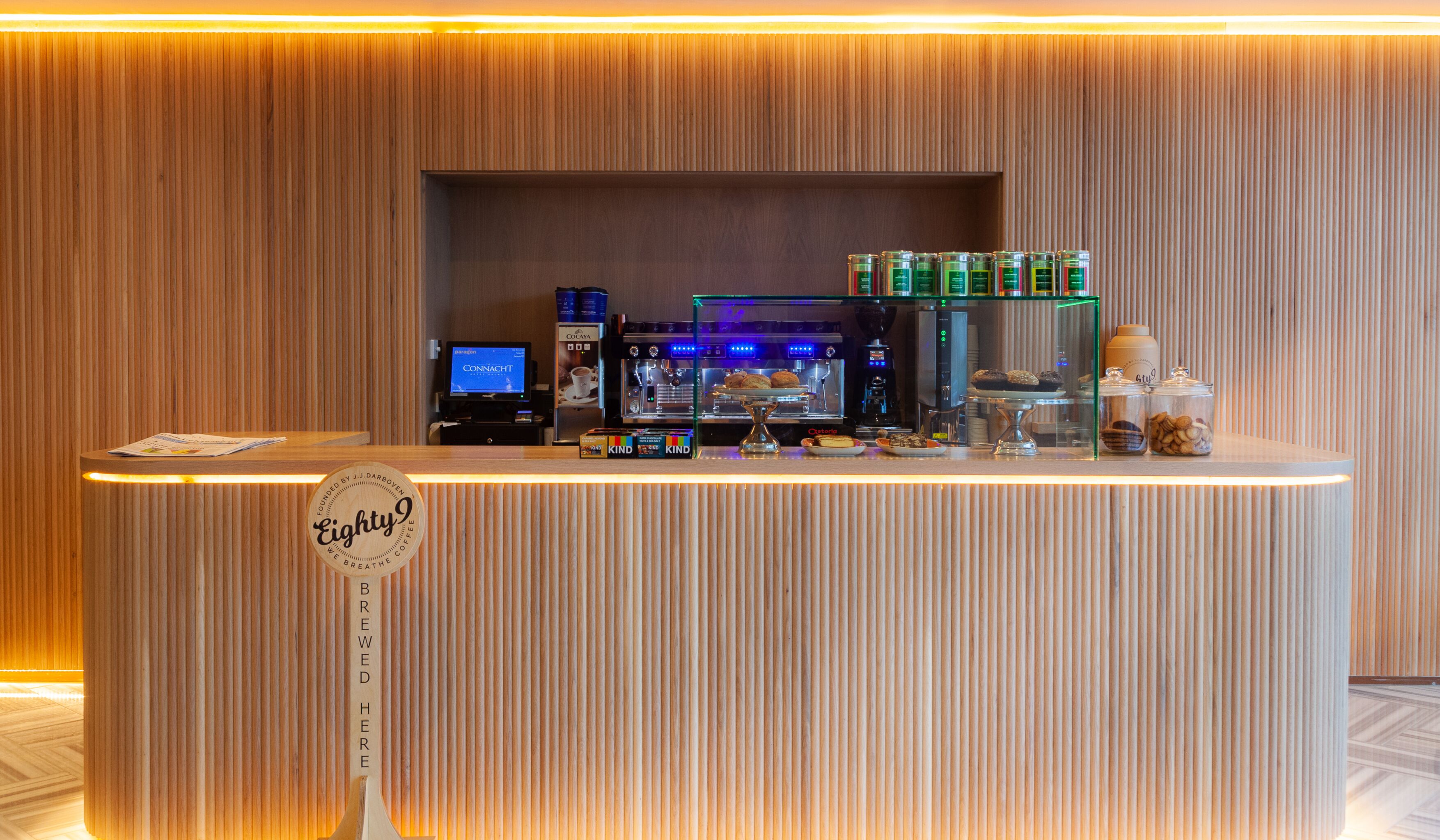 A coffee shop counter with a coffee machine, pastries, and a sign reading "Eighty Nine".