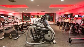A gym with multiple treadmills and stationary bikes, red lighting, and a digital display on the wall.