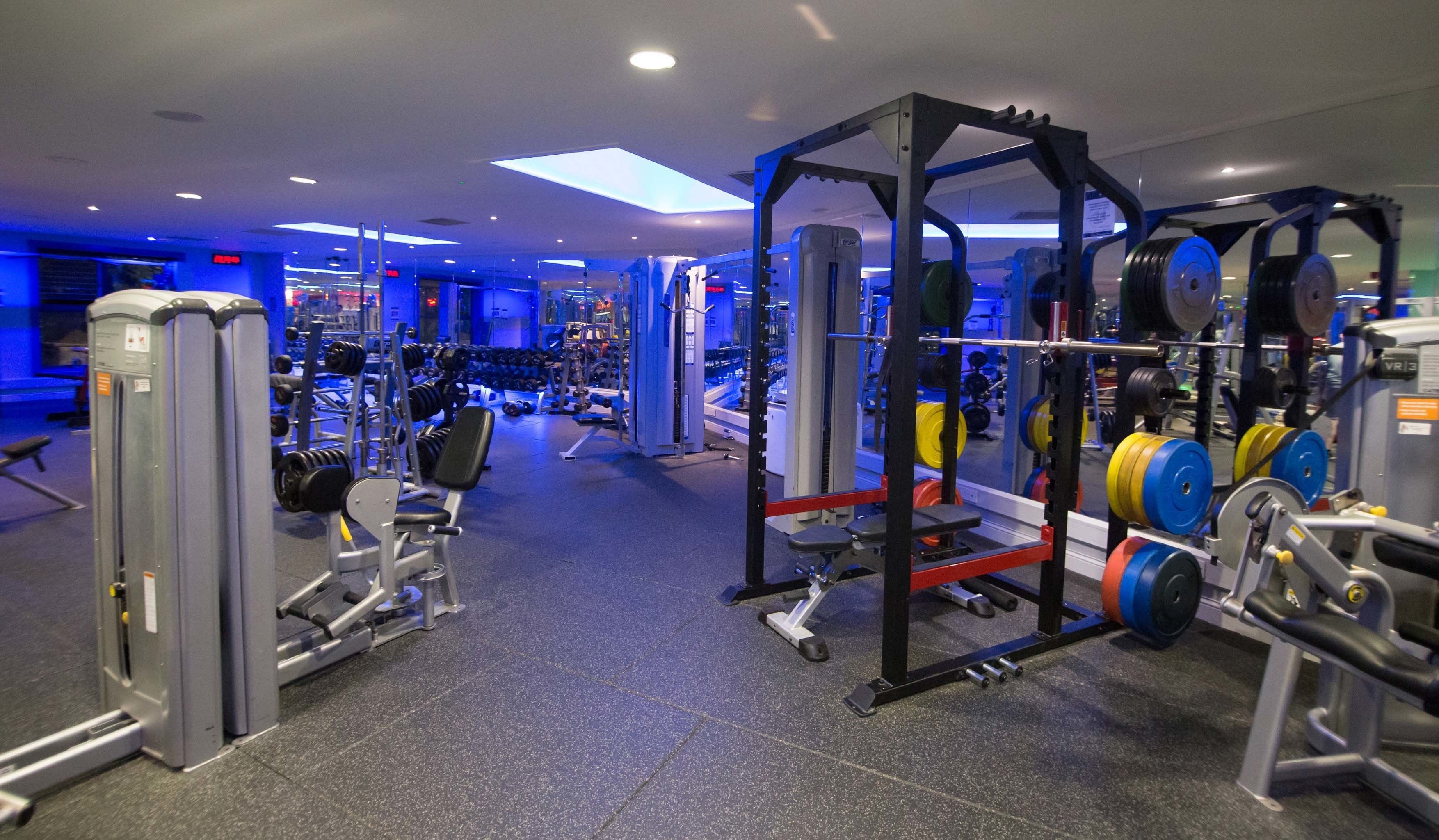 A gym with various exercise equipment, including weight machines, free weights, and a squat rack.