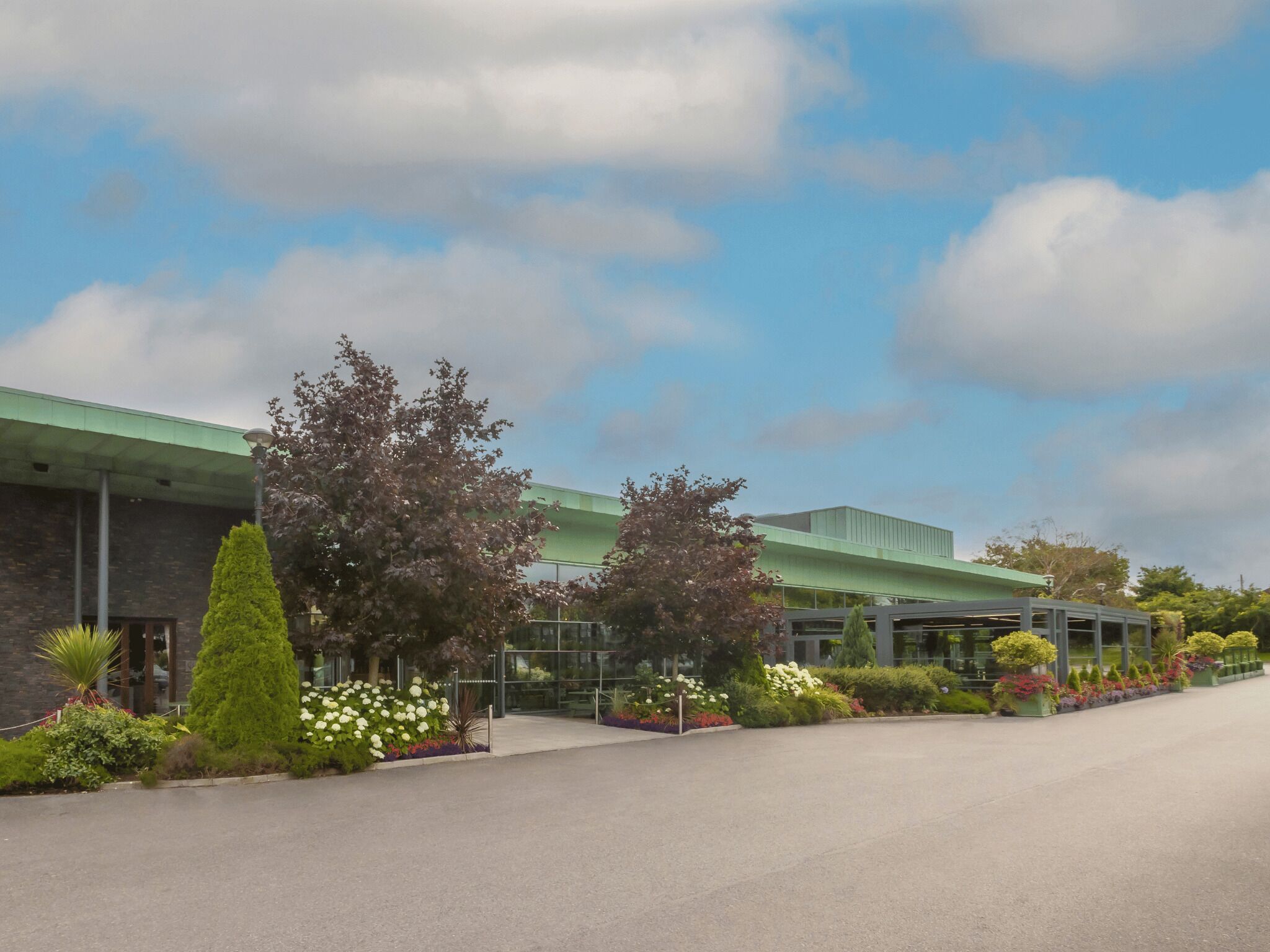 A modern building with a green roof, surrounded by well-maintained gardens and a paved walkway.
