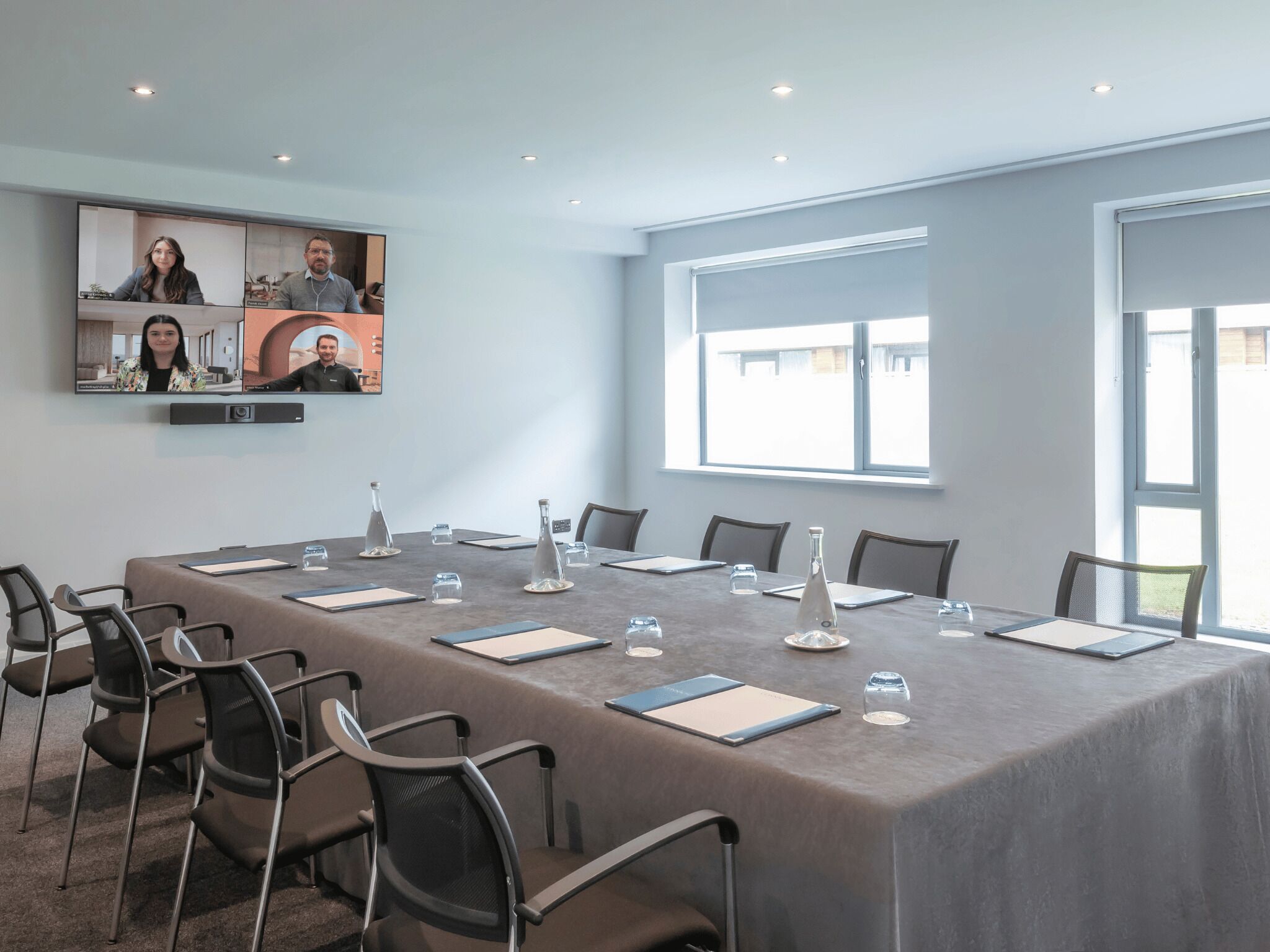 Une salle de conférence équipée d’une longue table, de chaises, d’un grand écran pour les vidéoconférences et de grandes fenêtres.