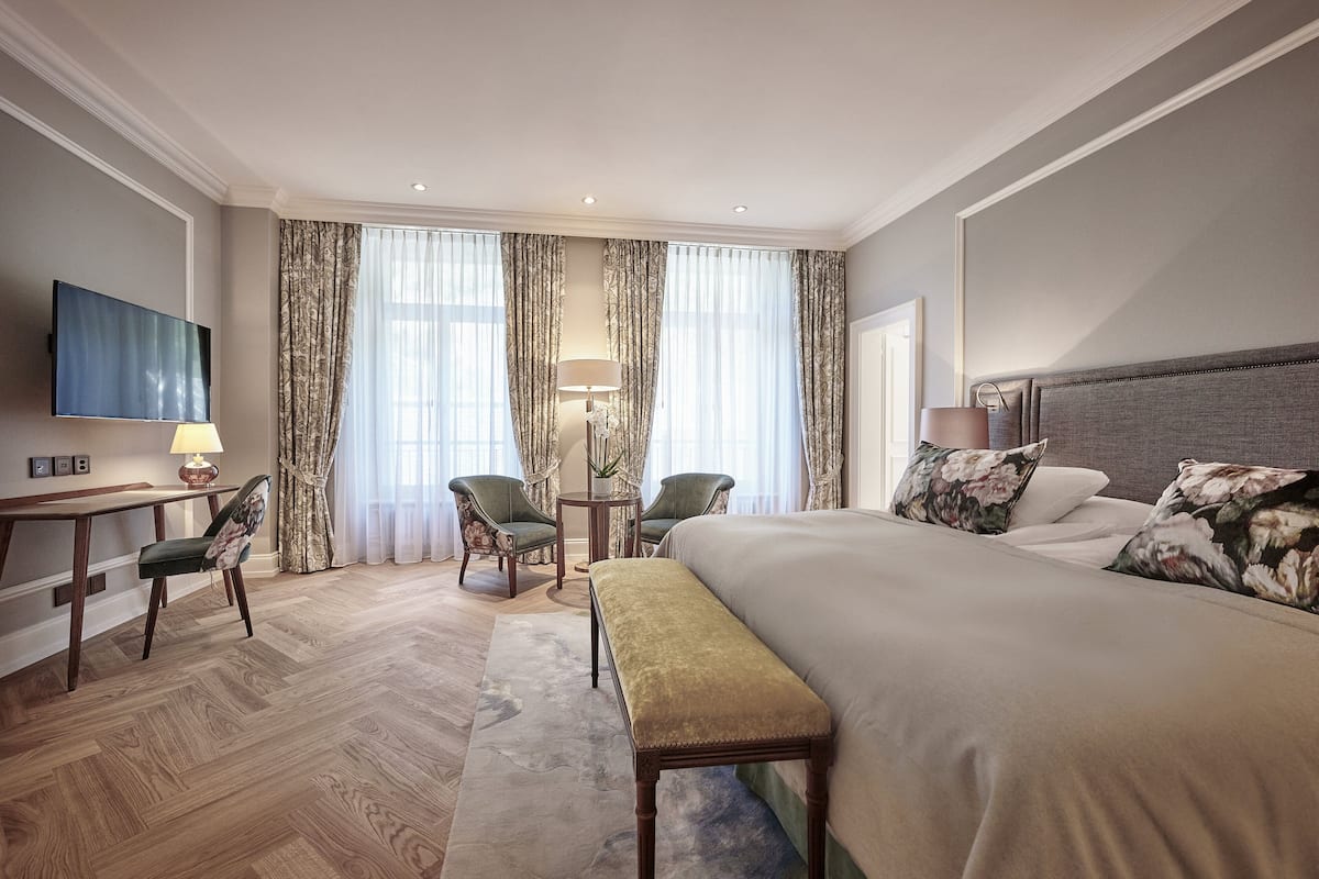 Habitación de hotel con una cama grande, un escritorio con silla, un televisor y dos sillas.