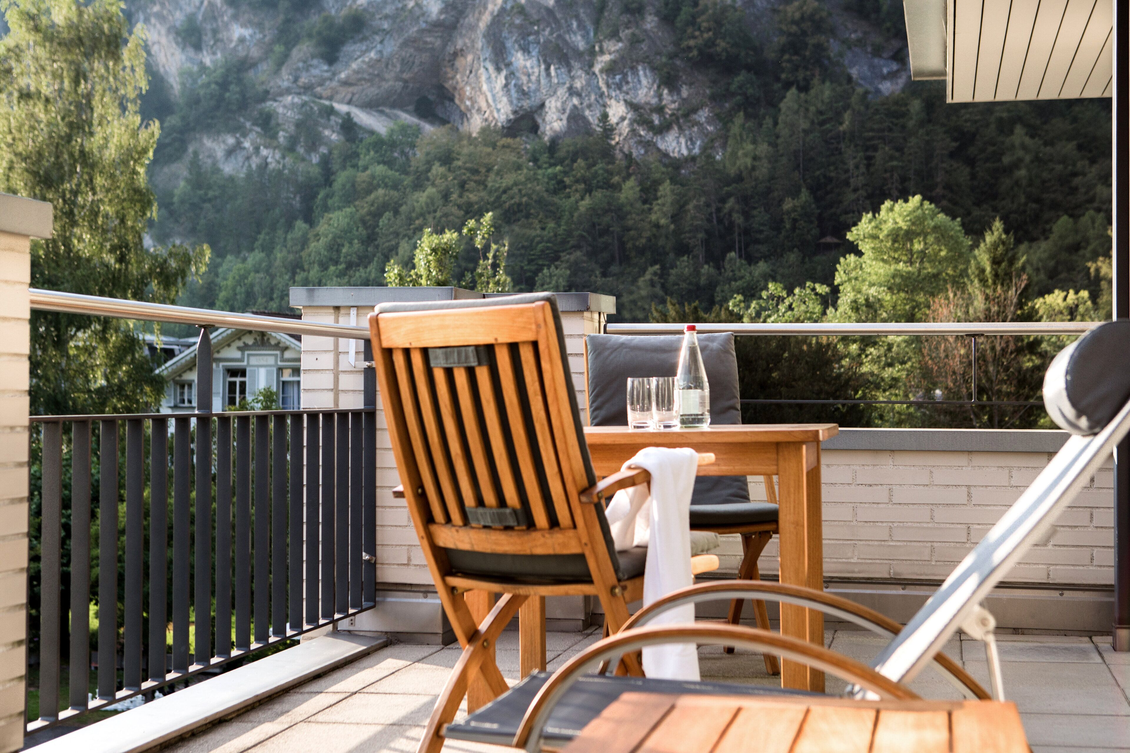 A balcony with a wooden chair and table, a bottle, and glasses.