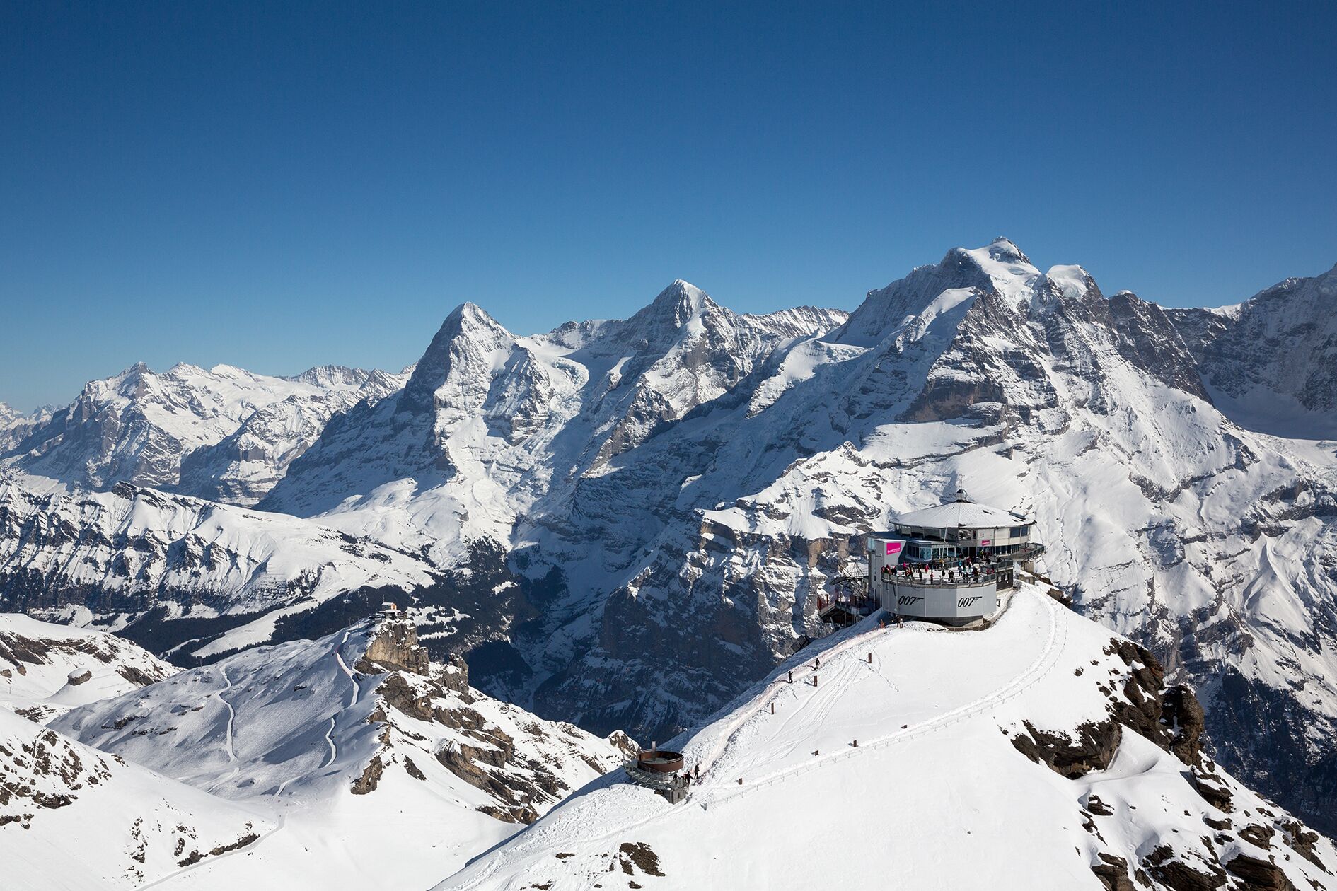 A snow-covered mountain with a chairlift and a building with a clear sky in the background.