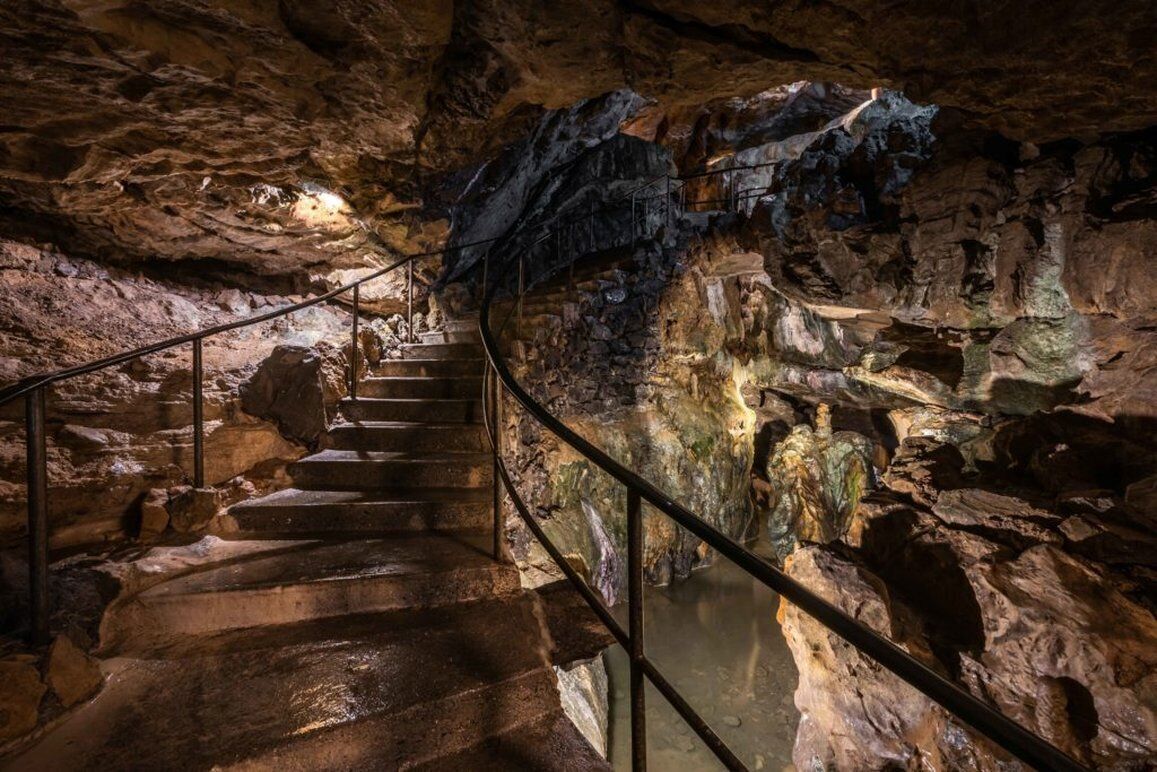 Una escalera en una cueva con barandales metálicos y formaciones rocosas naturales.