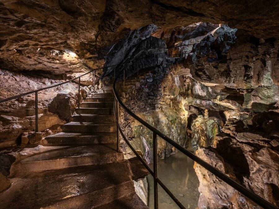 Una escalera en una cueva con barandales metálicos y formaciones rocosas naturales.