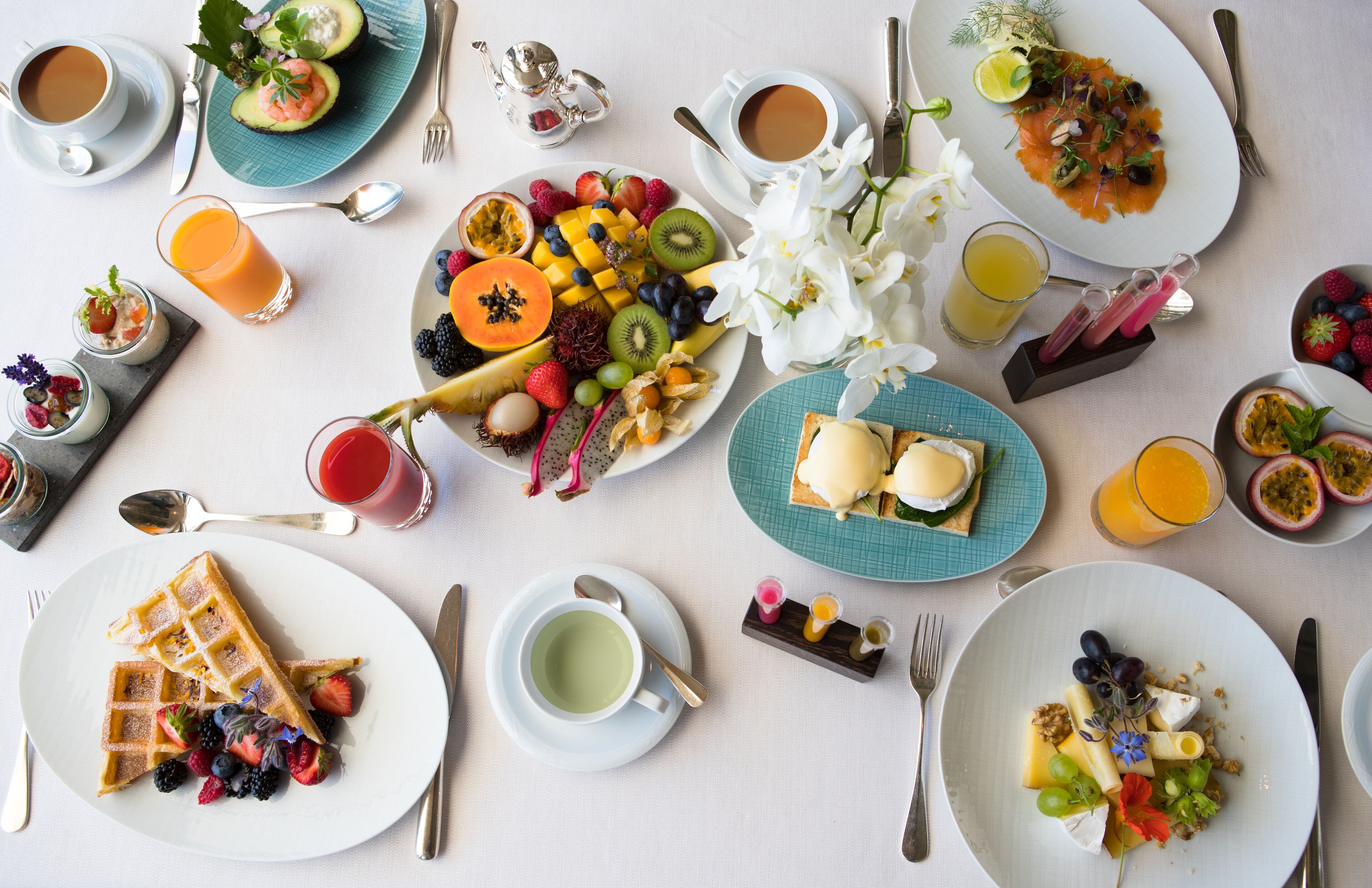 Disposição de pratos de café da manhã, incluindo waffles, frutas e ovos, sobre uma mesa.