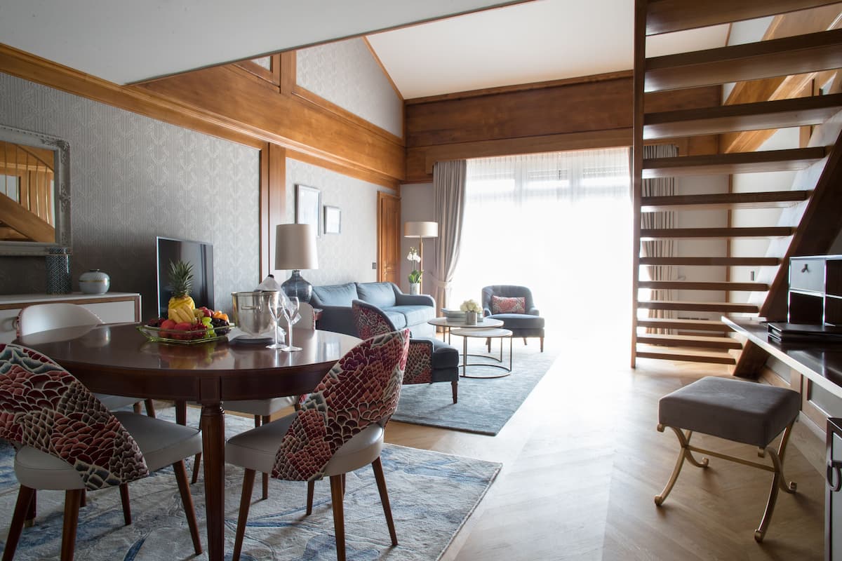 Una sala de estar moderna con comedor, que incluye una escalera de madera, un juego de sofás y una mesa de centro.