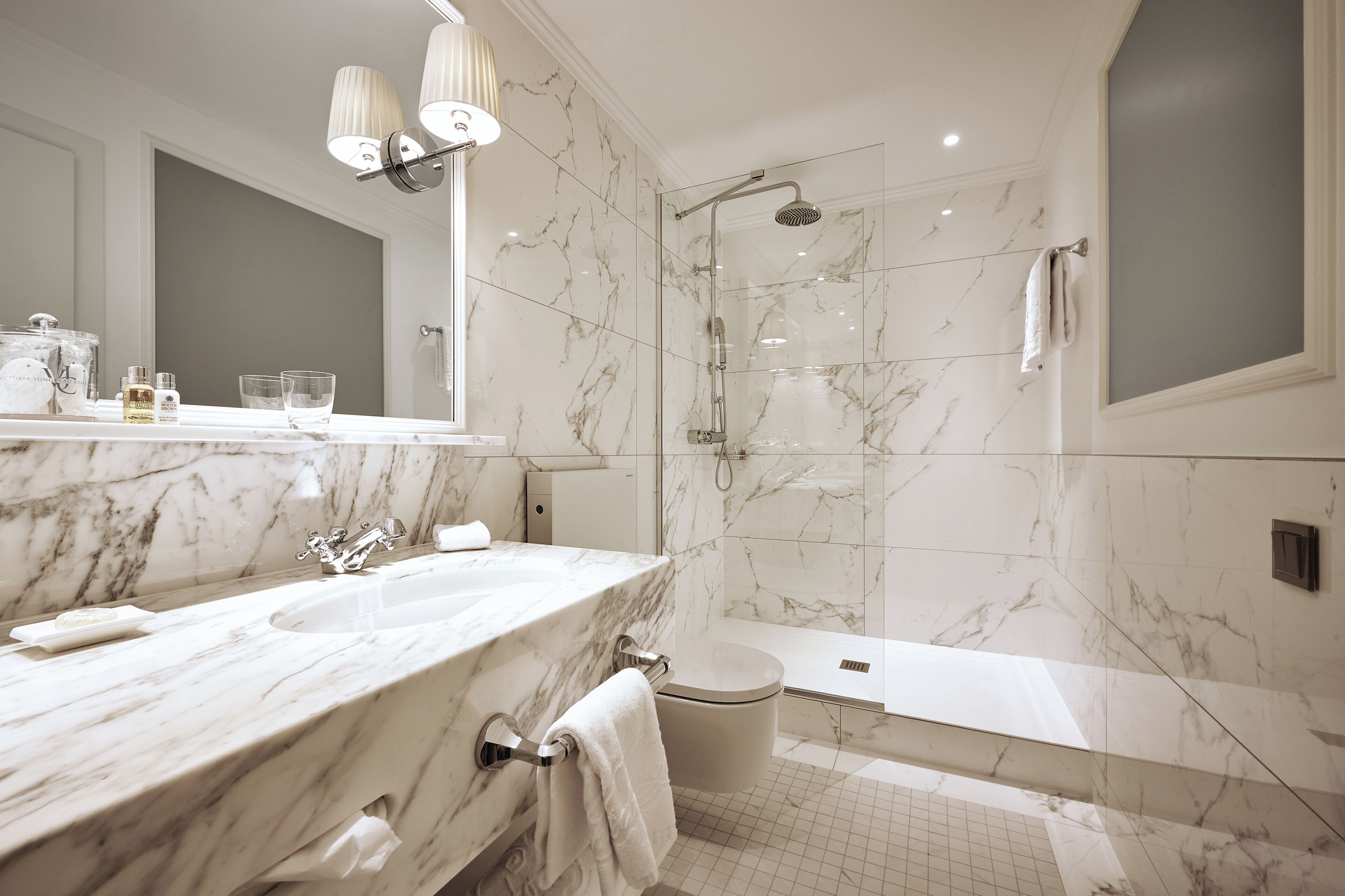 A modern bathroom with a marble vanity, a glass-enclosed shower, and a separate toilet.