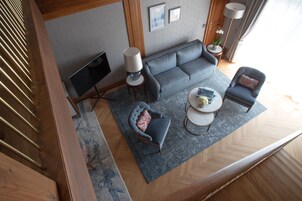 Un salón moderno con un sofá gris, dos sillones, una mesa de centro, un televisor y una lámpara.