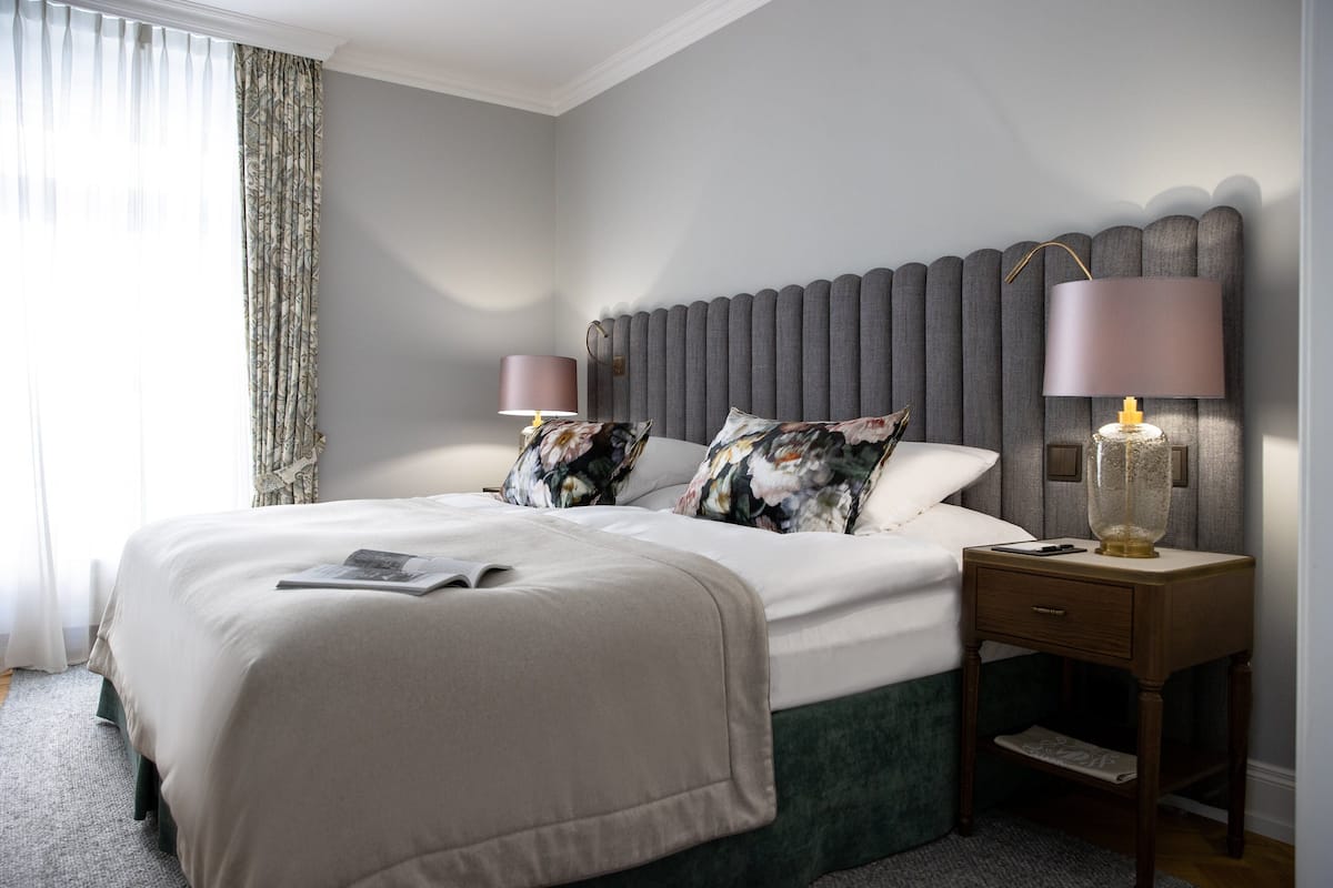 Un dormitorio ordenado con una cama grande, dos mesitas de noche con lámparas y un cabecero decorativo.