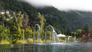 Ein Pool mit Wasserstrahlen, umgeben von üppiger Vegetation und einer Bergkulisse.