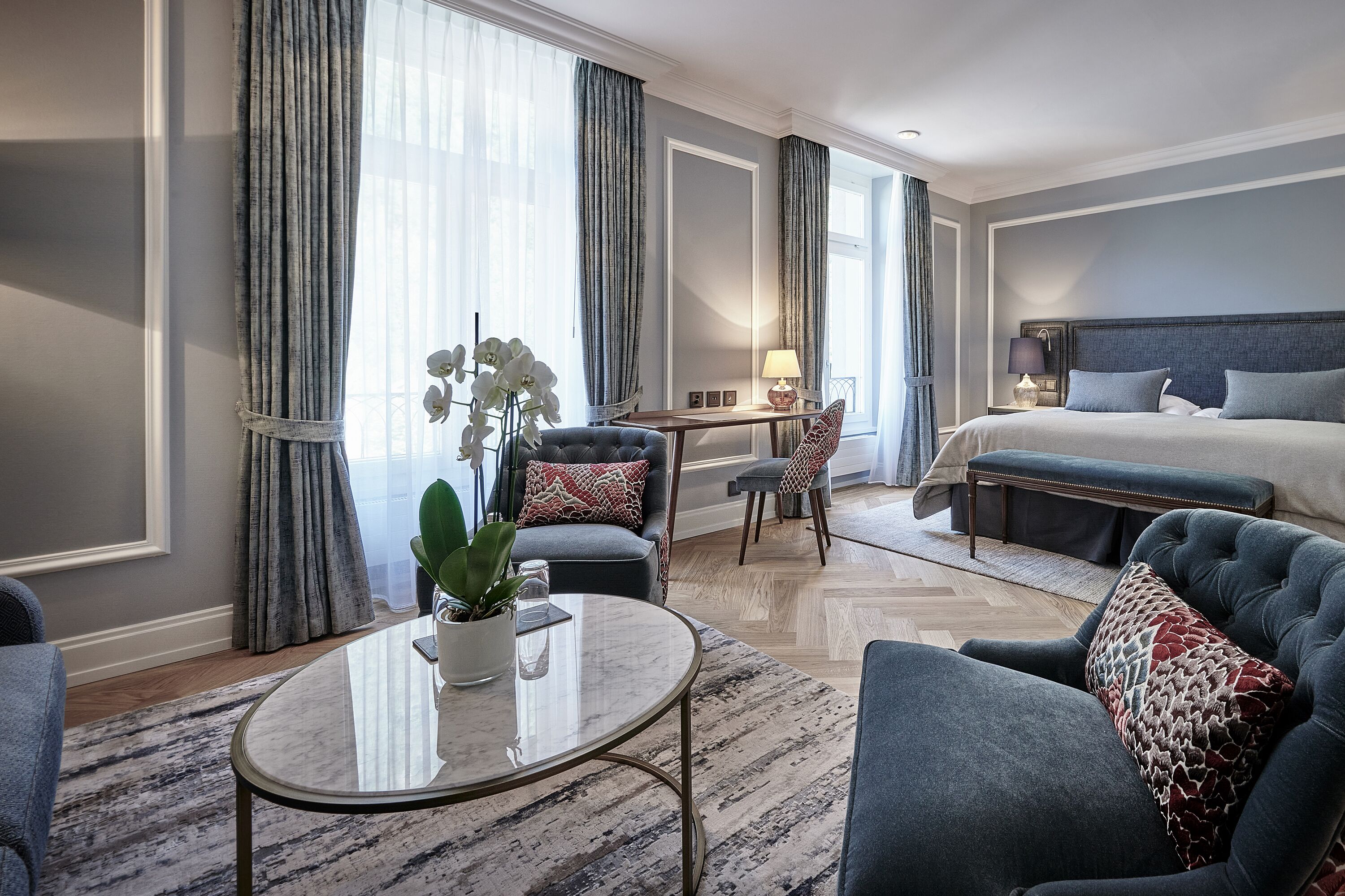 Ein modernes Hotelzimmer mit einem Bett, zwei Sesseln, einem kleinen Tisch und einem Schreibtisch.