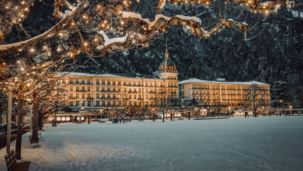 Ein großes Hotel mit mehreren Stockwerken und einer markanten Kuppel, umgeben von schneebedeckten Bäumen und einem verschneiten Innenhof.