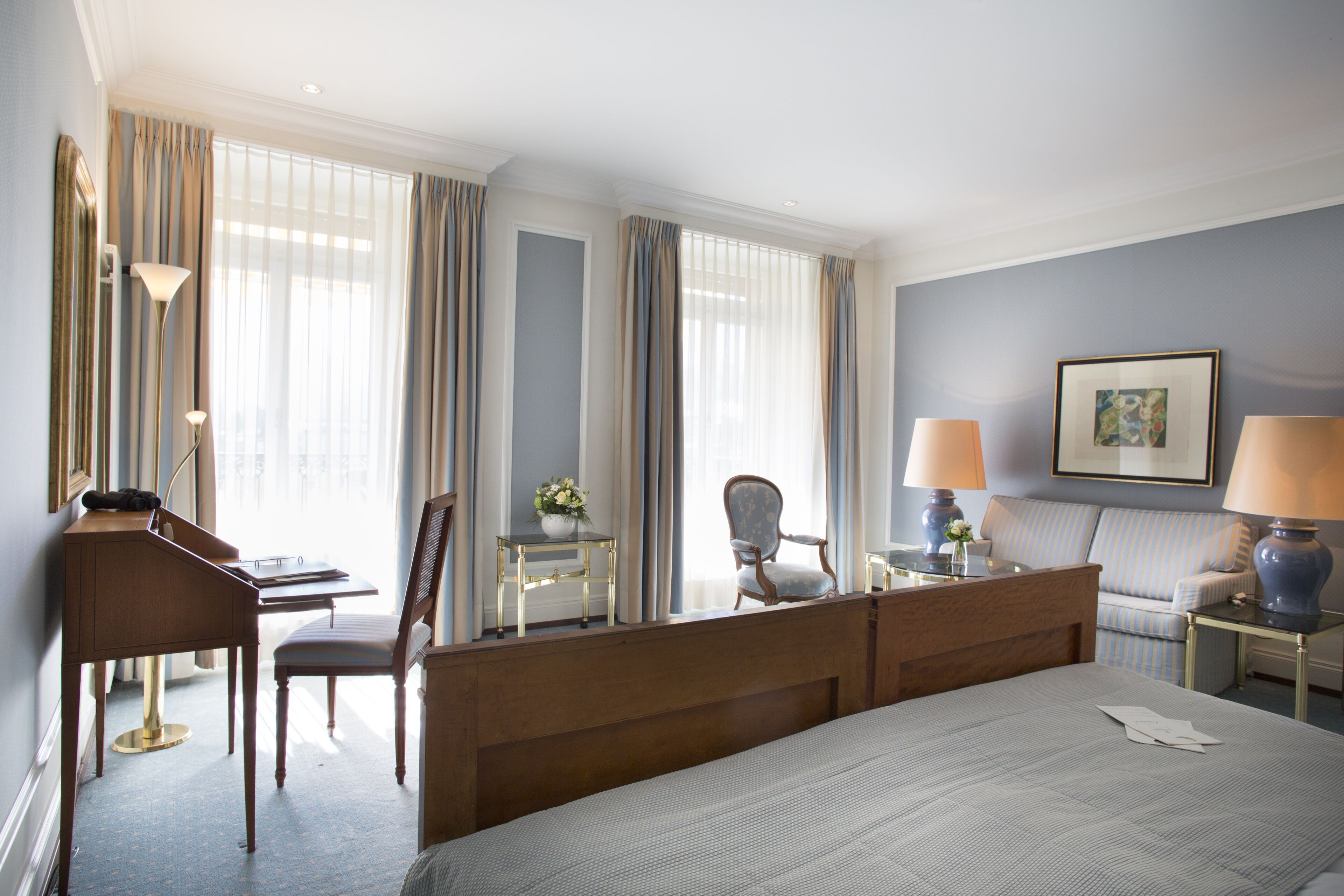 A hotel room with a bed, desk, chair, lamp, and a framed picture on the wall.