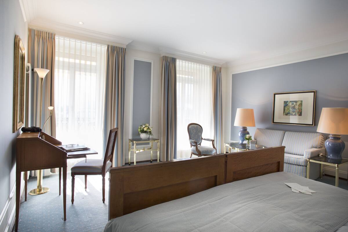 A hotel room with a bed, desk, chair, lamp, and a framed picture on the wall.