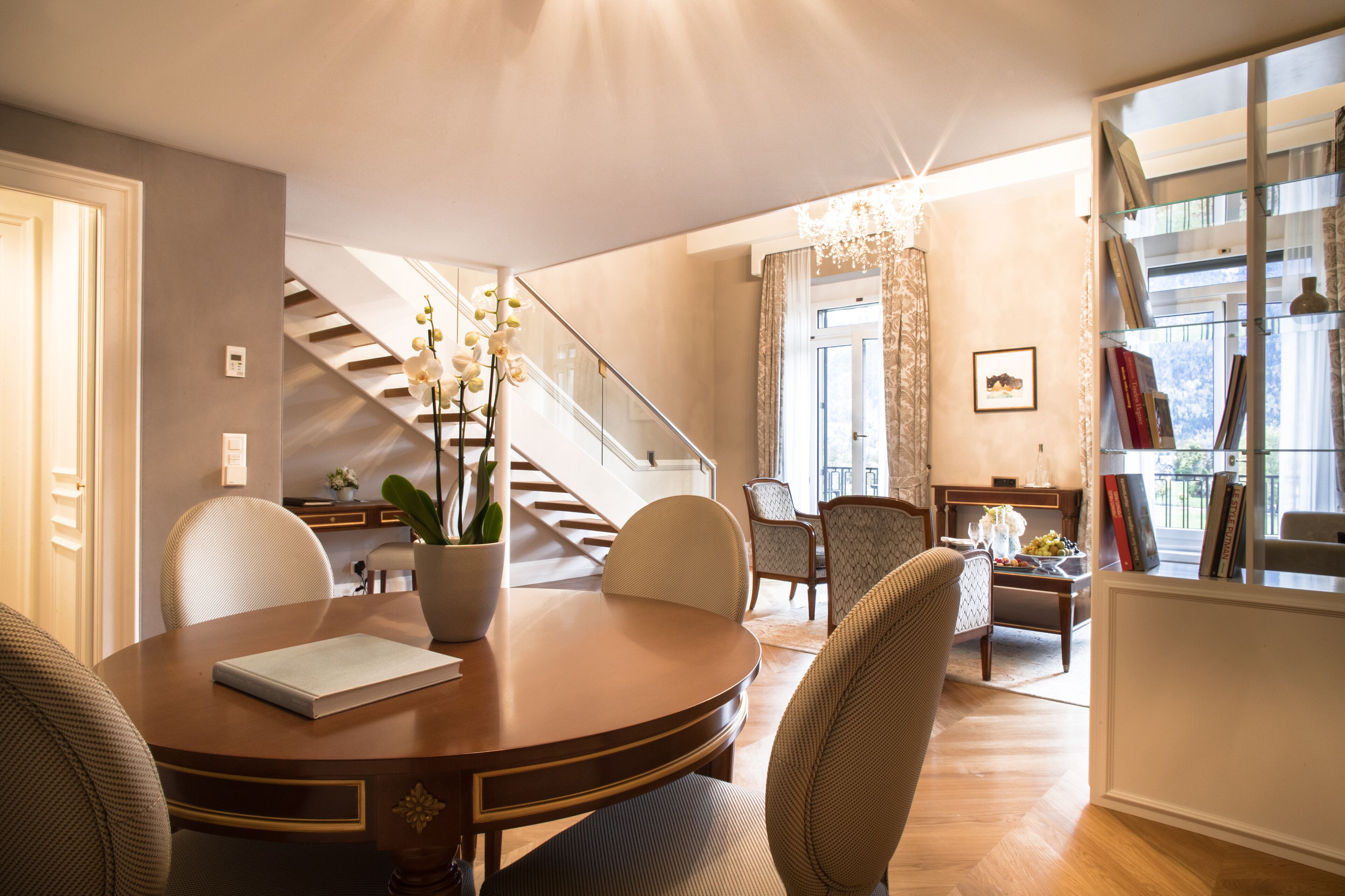 Ein modernes Wohnzimmer mit einem runden Holztisch, gemütlicher Sitzgelegenheit, einer Treppe und einem Balkon mit Bücherregalen.