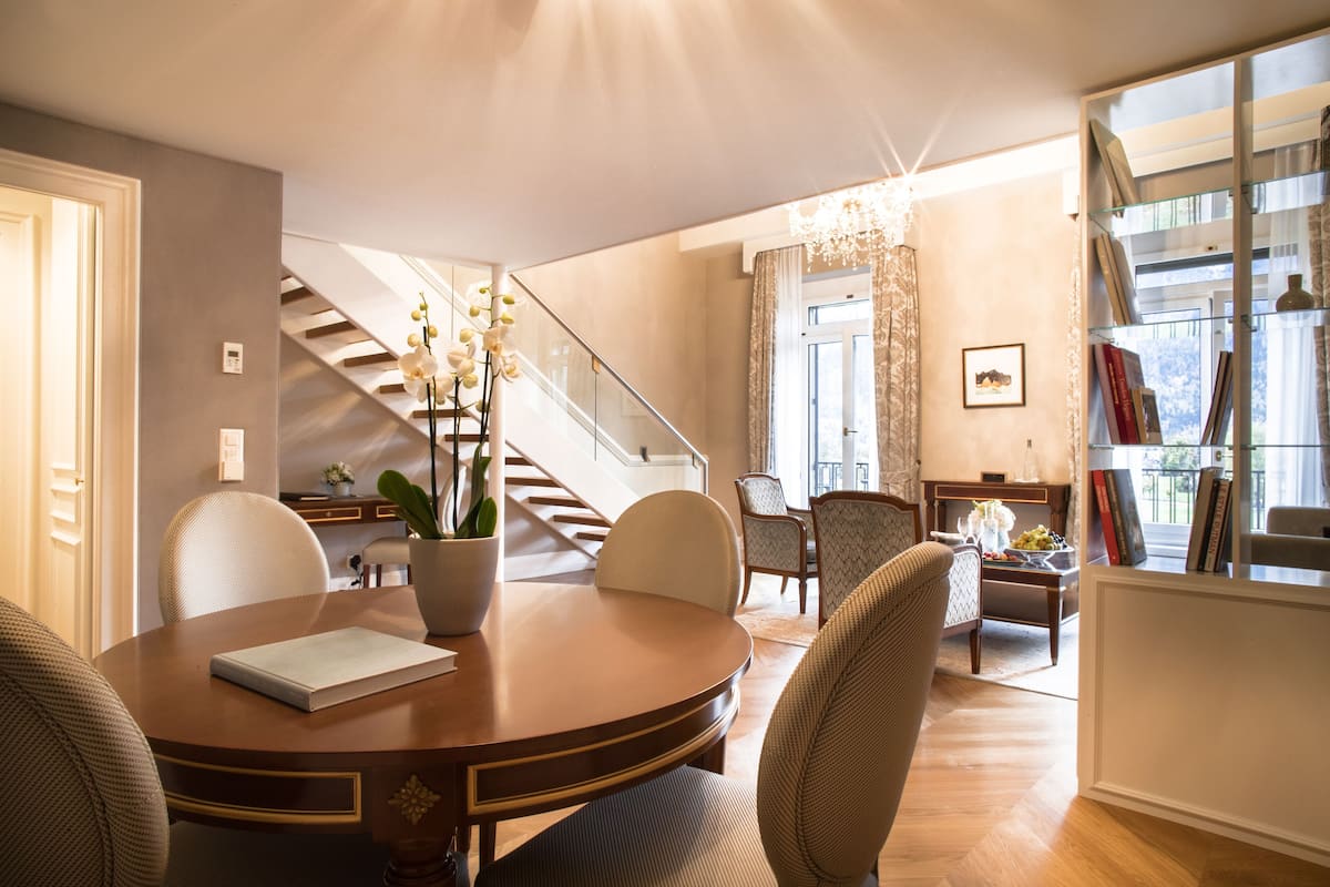Una sala de estar moderna con una mesa redonda de madera, asientos cómodos, una escalera y un balcón con estanterías.