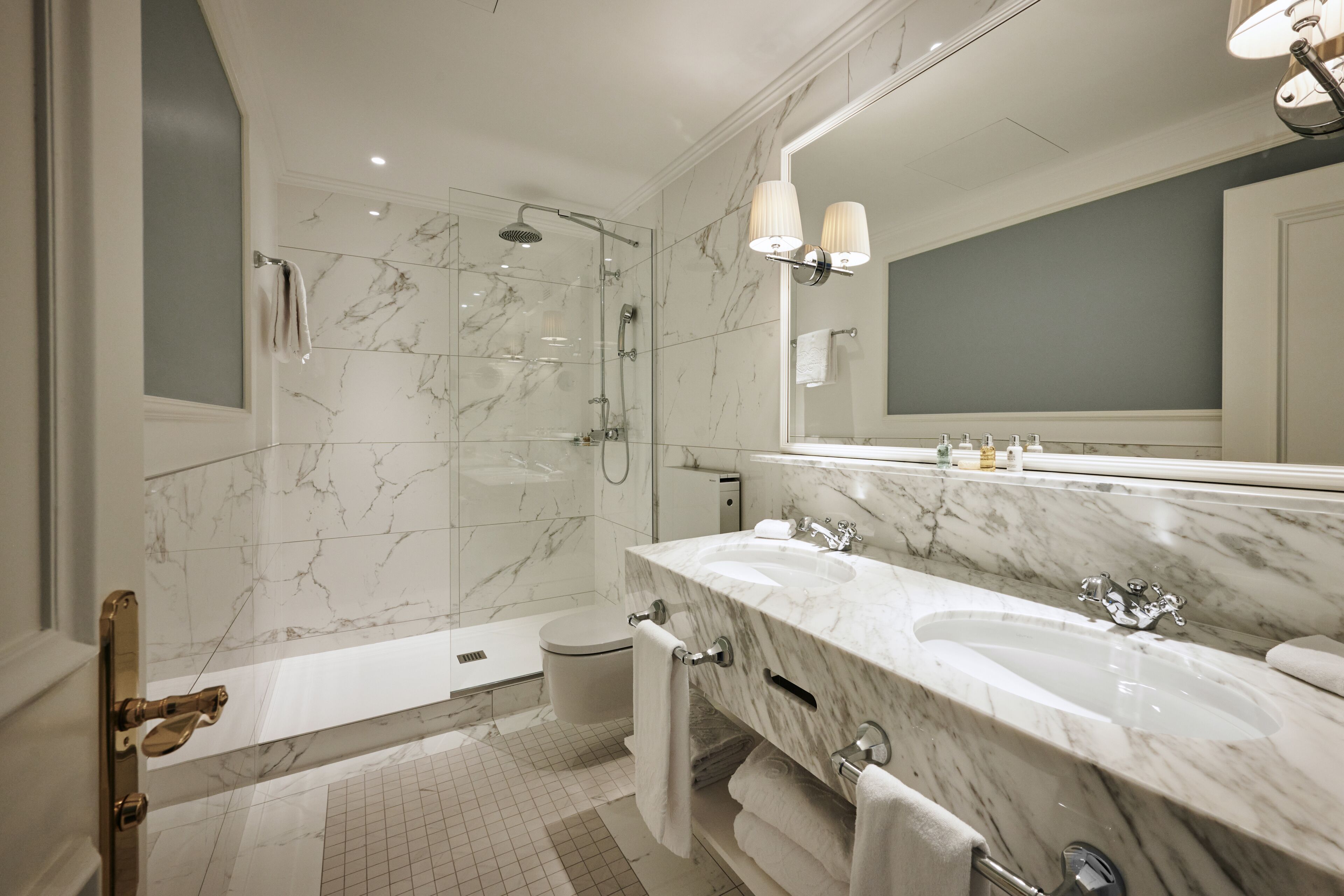 Un baño moderno con ducha de vidrio, un tocador amplio con dos lavamanos y un espejo grande.