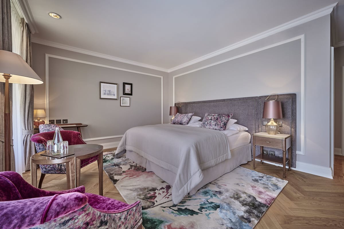 Un dormitorio con una cama grande, una mesita de noche con lámpara, una silla y una pequeña mesa con lámpara.