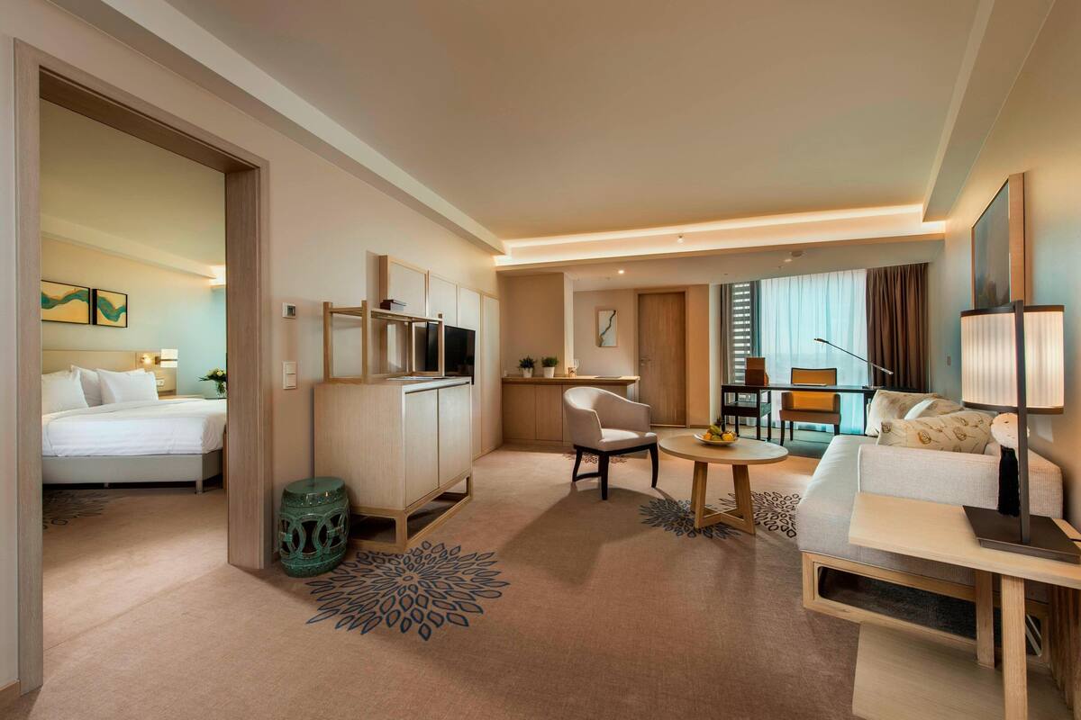 A hotel room with a bed, a desk, a chair, a sofa, and a dining table.