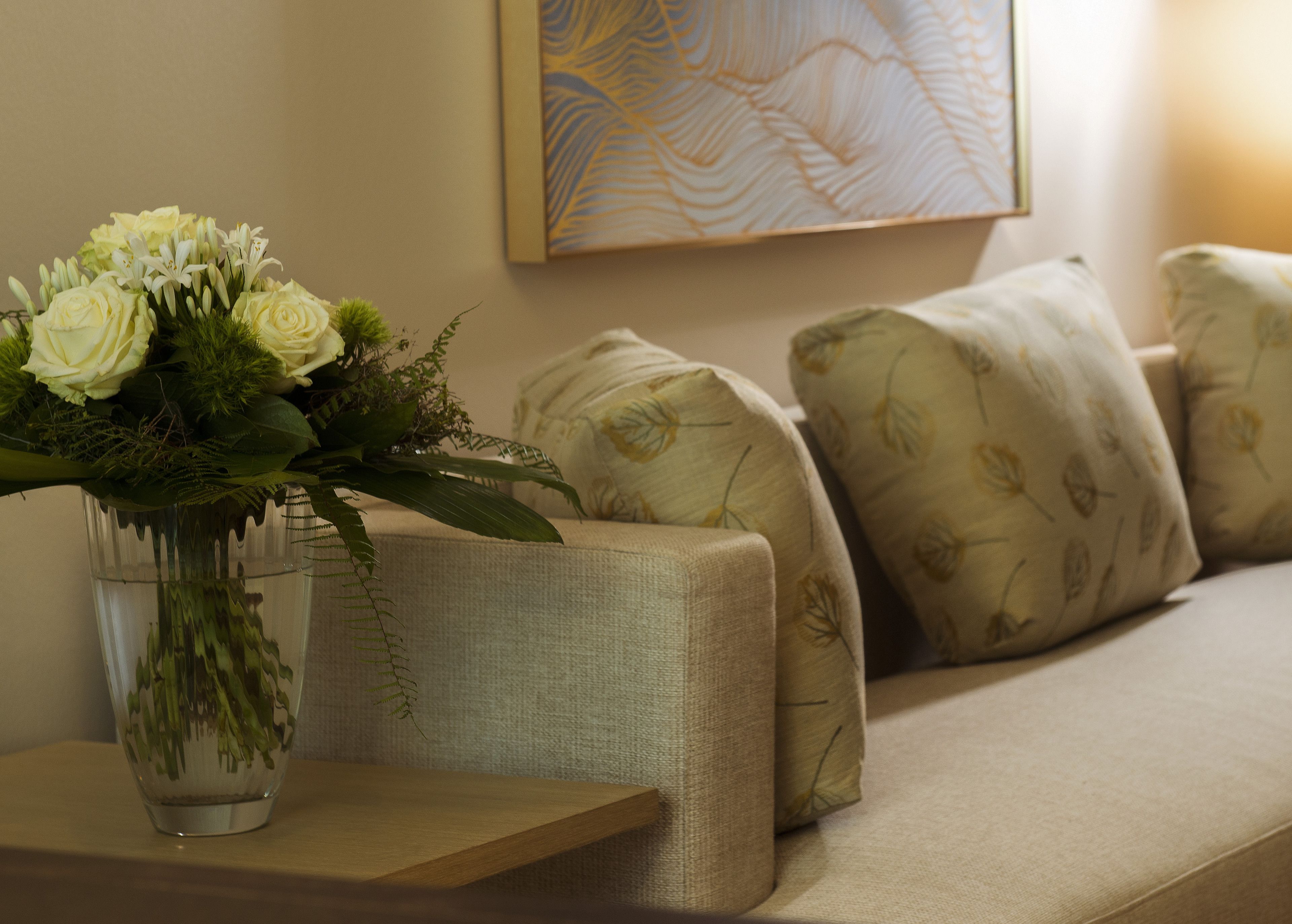 A living room with a sofa, a glass vase with flowers, and a painting on the wall.