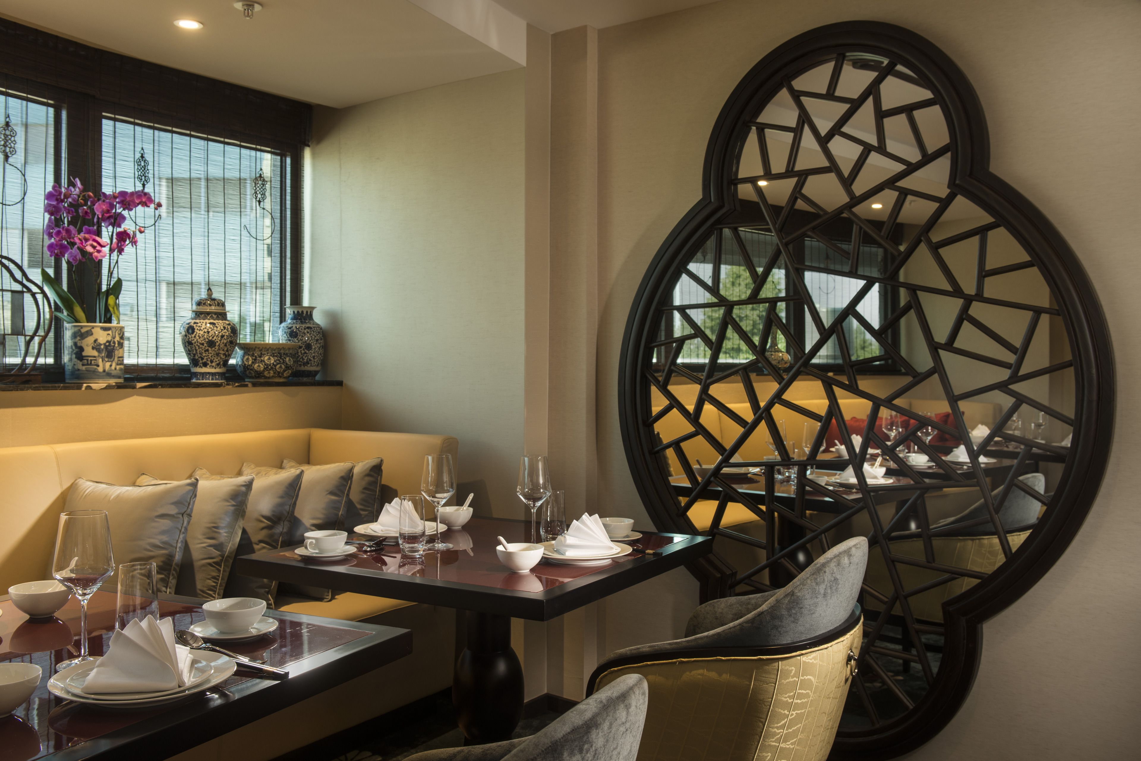 A dining area with a round table set for two, a sofa with cushions, and a decorative window with a geometric pattern.