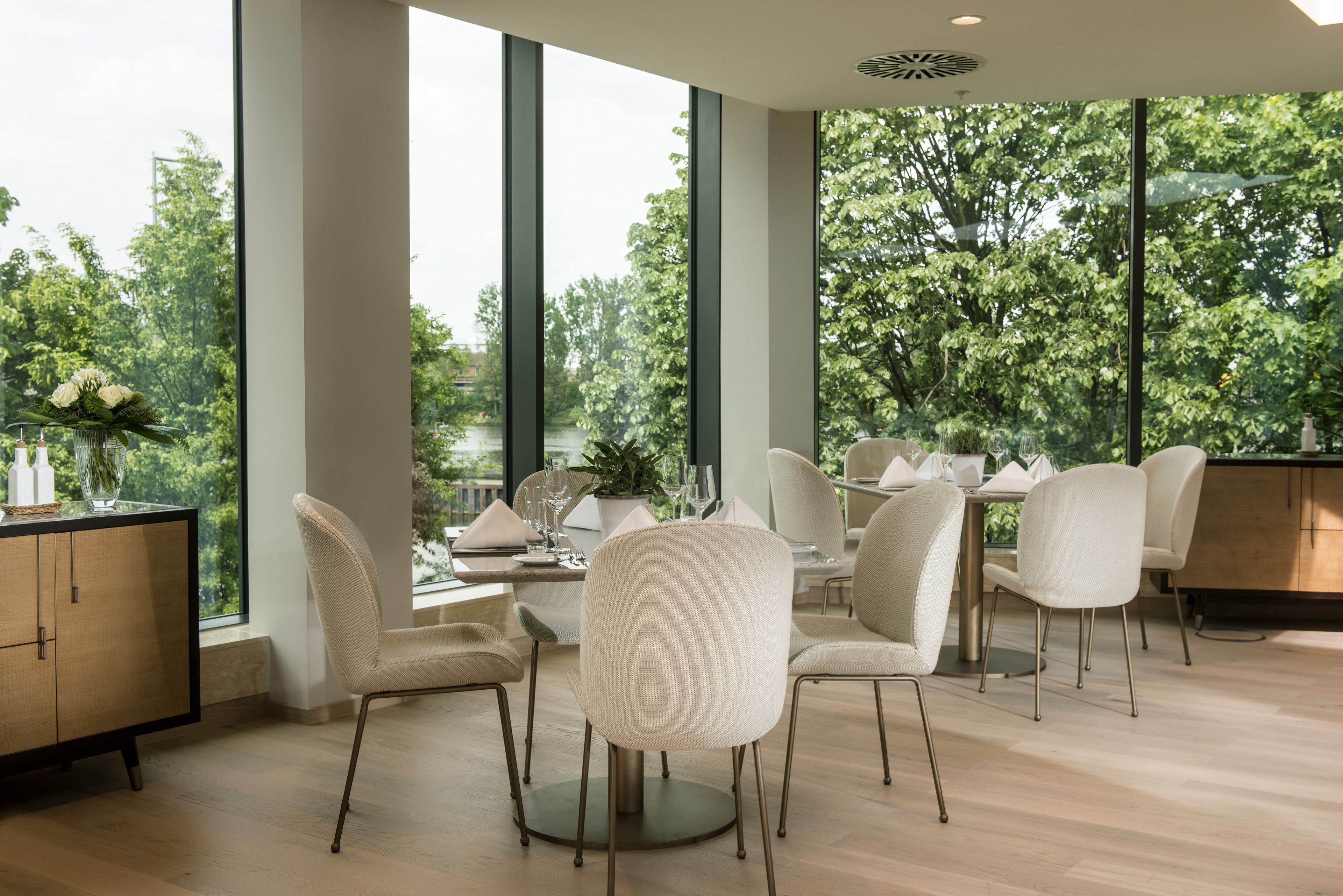 A modern dining area with large windows, wooden flooring, and contemporary chairs.