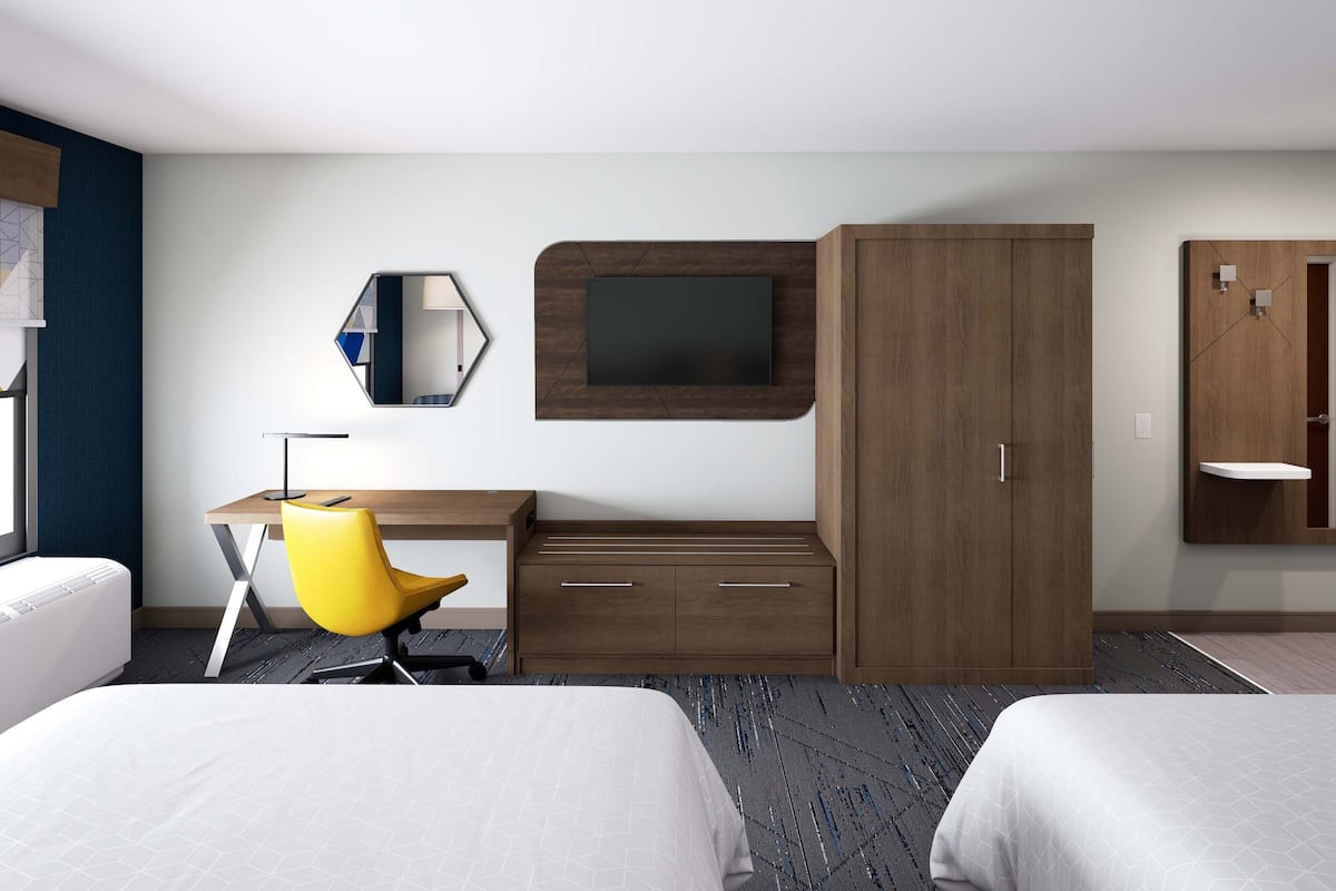 A hotel room with two beds, a desk with a chair, a TV mounted on a wooden panel, and a wardrobe.
