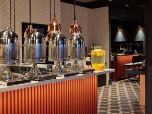 A bar area with copper and glass beverage dispensers, a large glass jar with citrus slices, and a patterned floor. - Hotel Caledonien (Kristiansand)