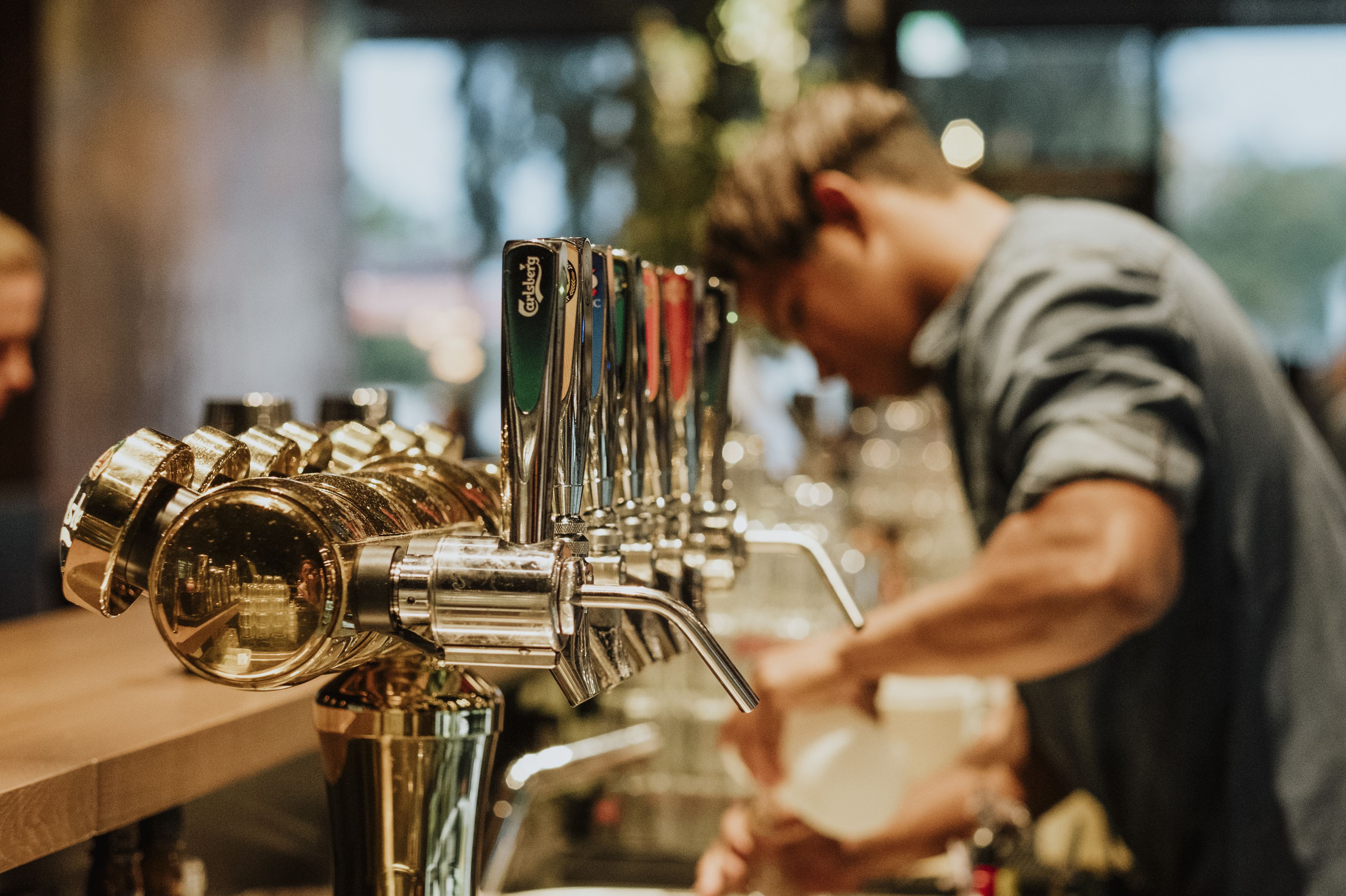 A bar with a row of taps and a person preparing drinks.